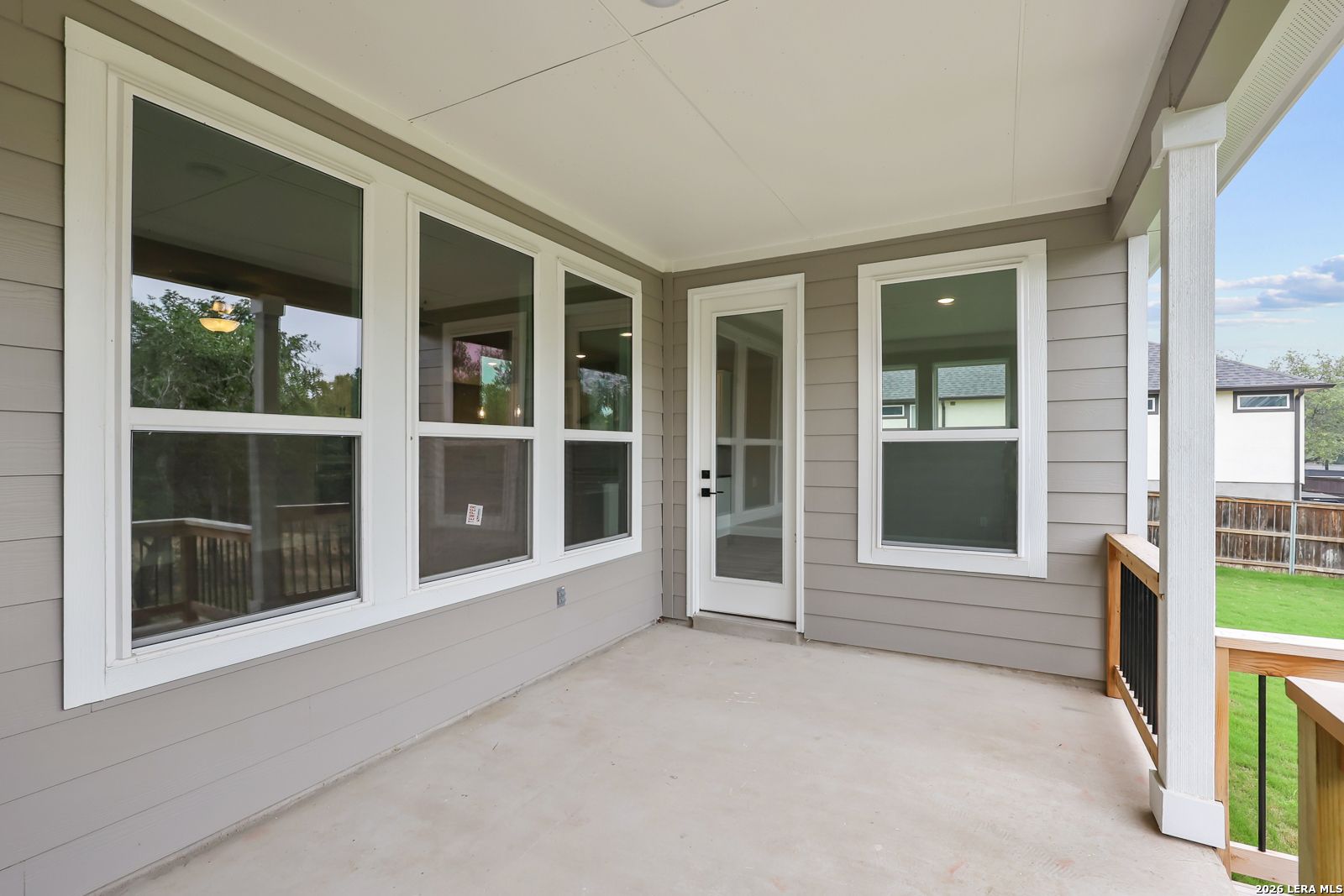 Covered back porch with large windows, glass door, and wooden deck overlooking lush green yard in Davidson Homes The Belmont H, Castroville, Texas