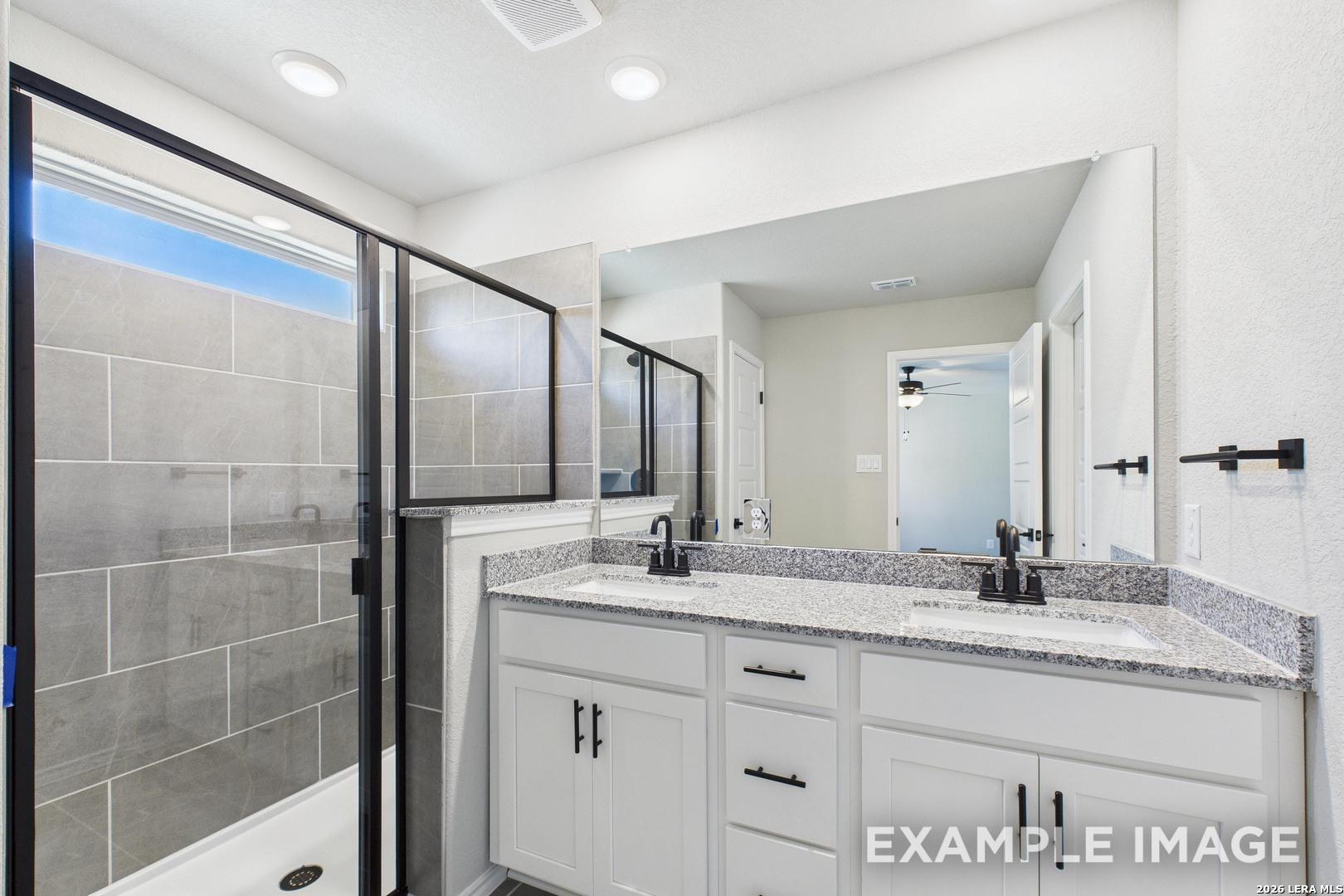 Modern bathroom with double vanity, granite countertops, and tiled walk-in shower in The Charlotte B, Cedar Heights, TX.