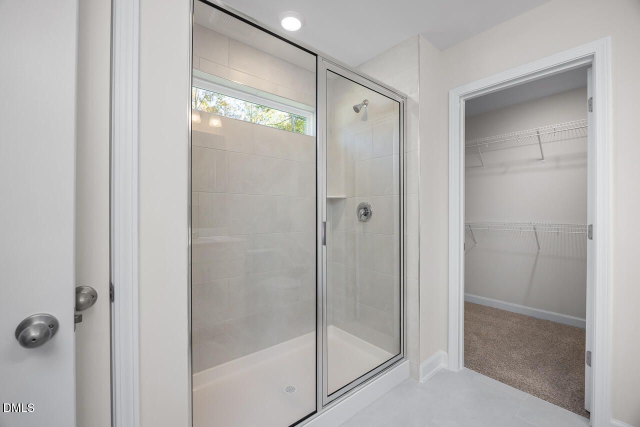 Modern frameless glass walk-in shower with rain showerhead and niche in master bath, adjacent walk-in closet in The Grace C home, Lillington, NC