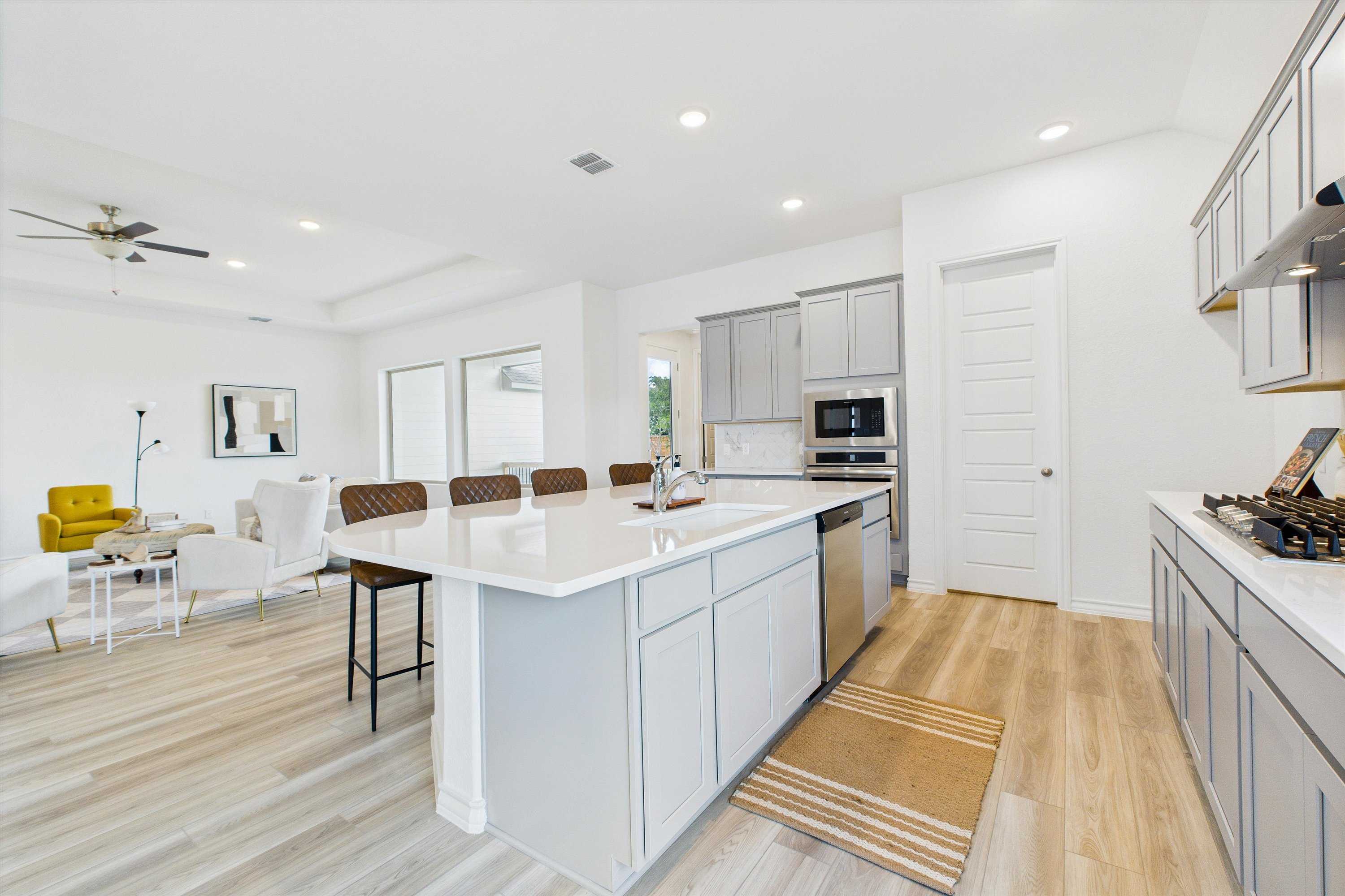 Modern open-concept kitchen with white island, stainless appliances, and dining area in The Summerlin C by Davidson Homes, Castroville, Texas