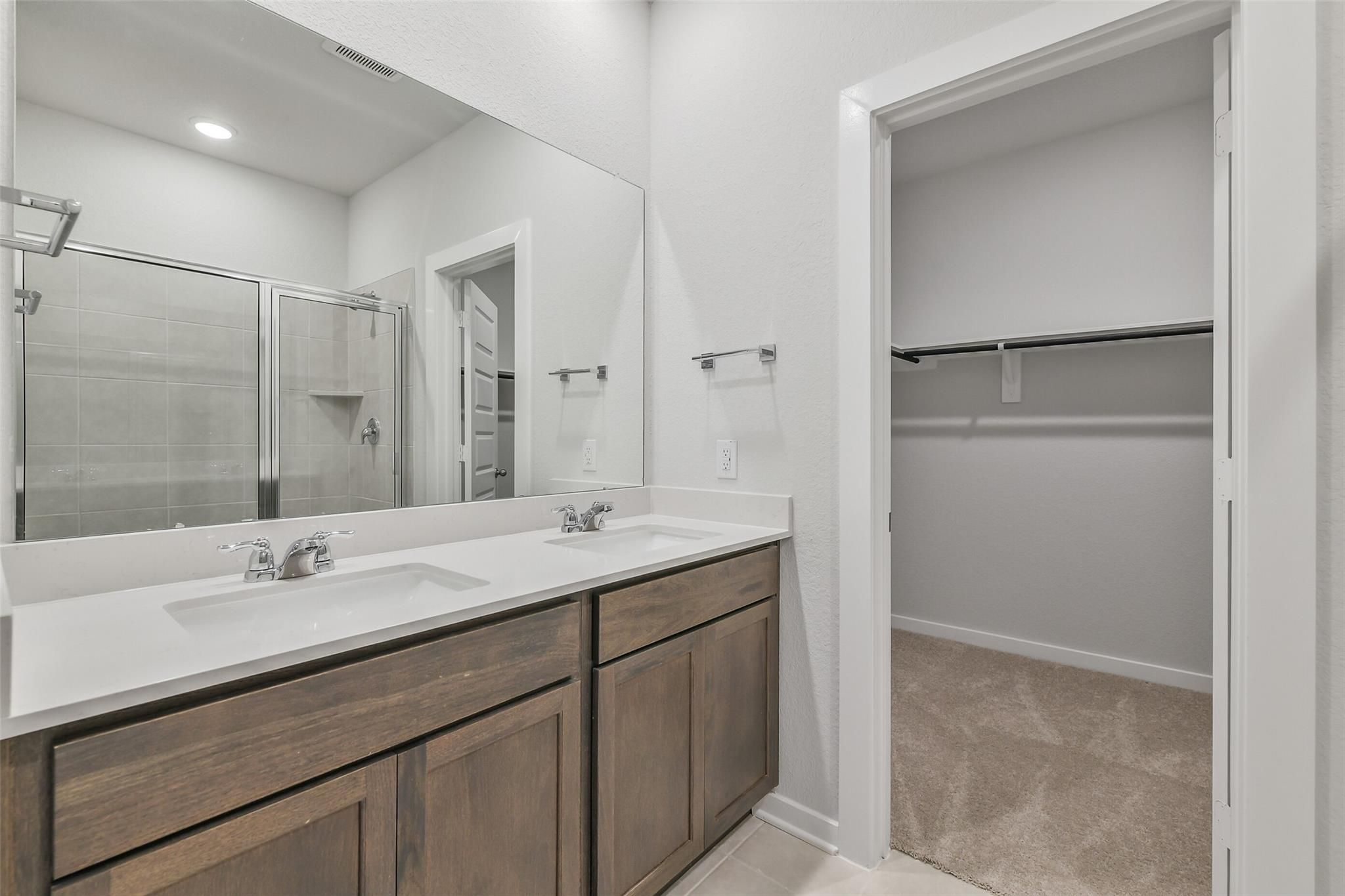 Modern master bathroom featuring double vanity, glass shower enclosure, and adjacent walk-in closet in Davidson Homes The Brazos E, Cleveland, Texas