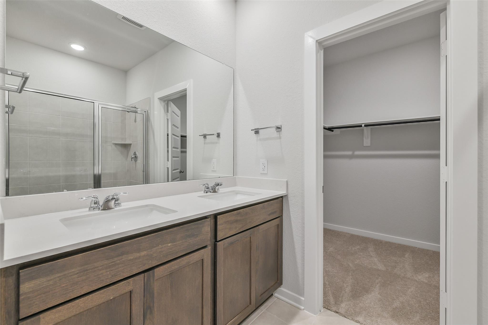 Modern master bathroom featuring double vanity, glass shower enclosure, and adjacent walk-in closet in Davidson Homes The Brazos E, Cleveland, Texas
