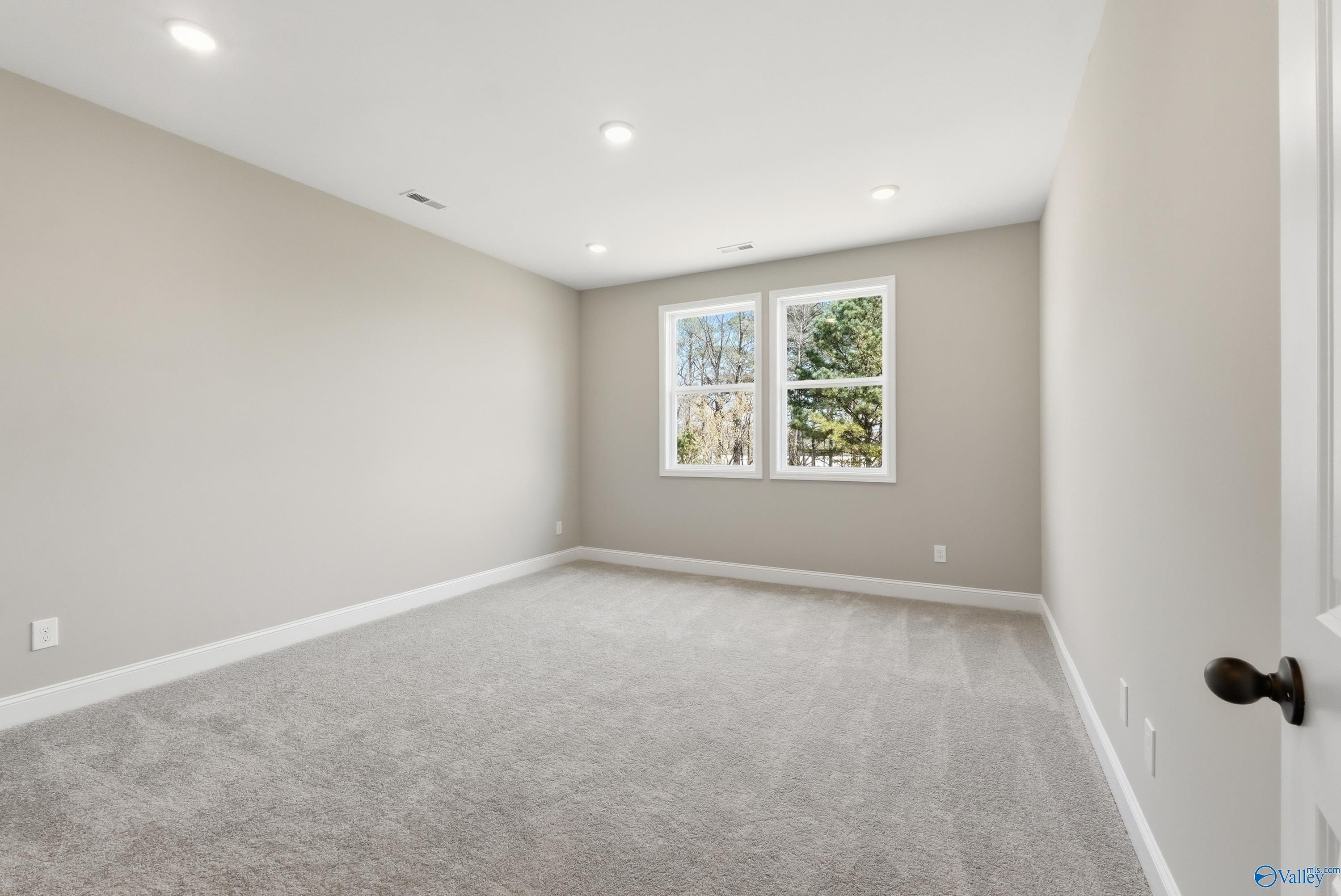 Spacious empty bedroom with large windows, beige walls, plush carpet, and recessed lights in Davidson Homes The Laurel K, Cullman, Alabama