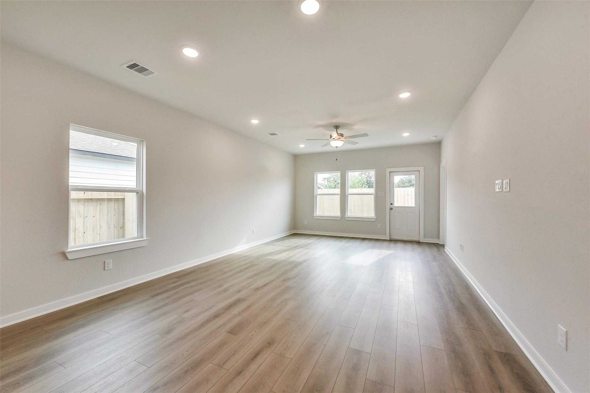 Spacious empty living room with wood laminate floors, ceiling fan, large windows, and patio doors in Davidson Homes The Frio G, Dayton, Texas