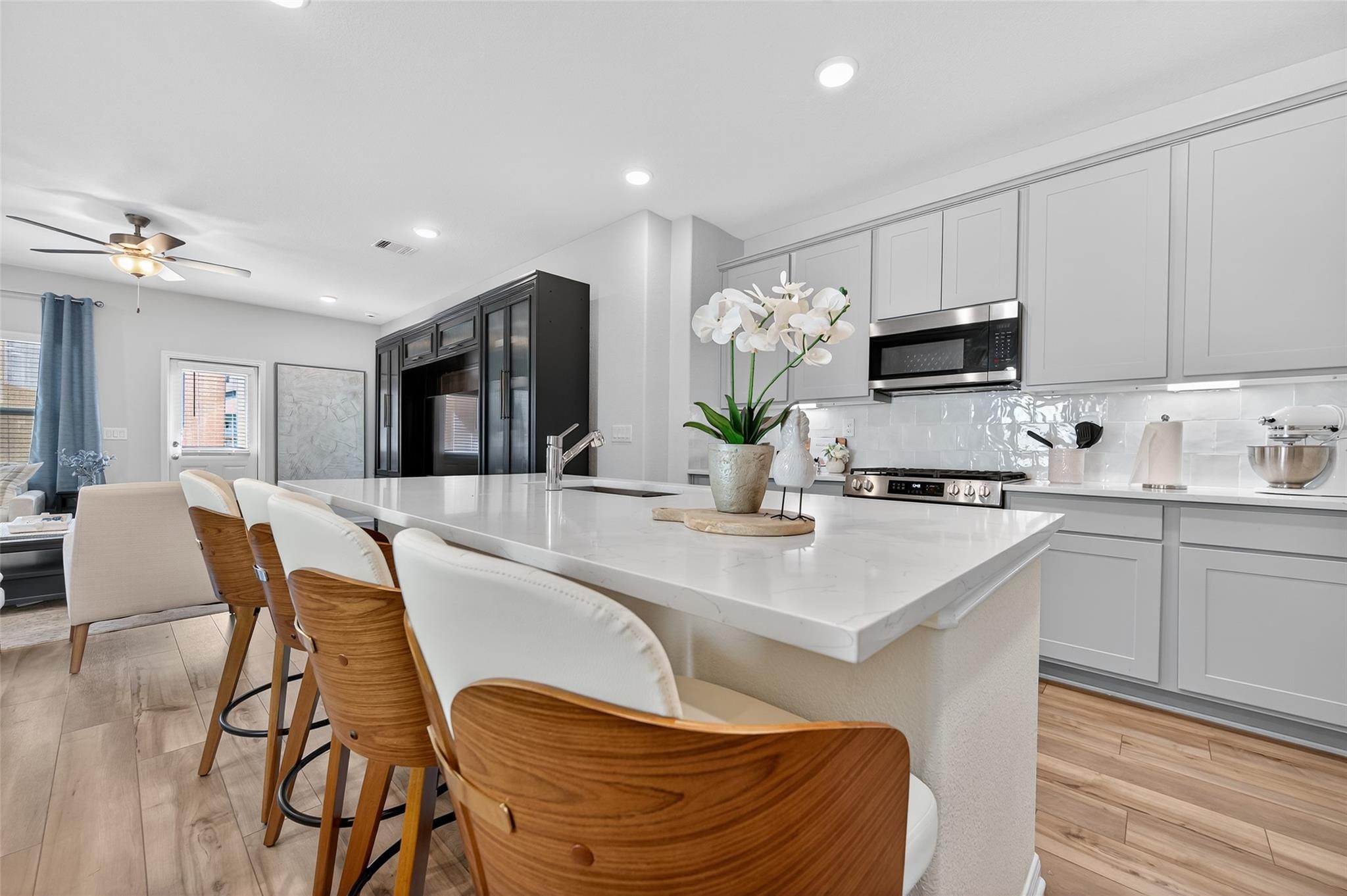 Modern kitchen island with white quartz counters, gray shaker cabinets, stainless appliances, and orchids in The Brazos E by Davidson Homes, Magnolia, TX