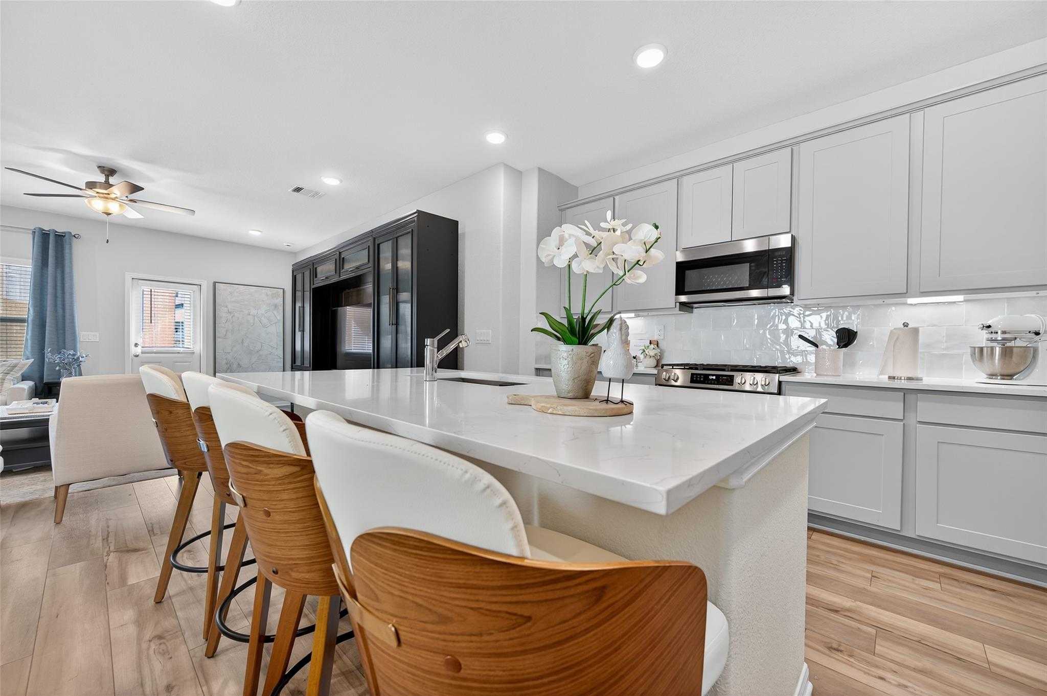 Modern kitchen island with white quartz counters, gray shaker cabinets, stainless appliances, and orchids in The Brazos E by Davidson Homes, Magnolia, TX