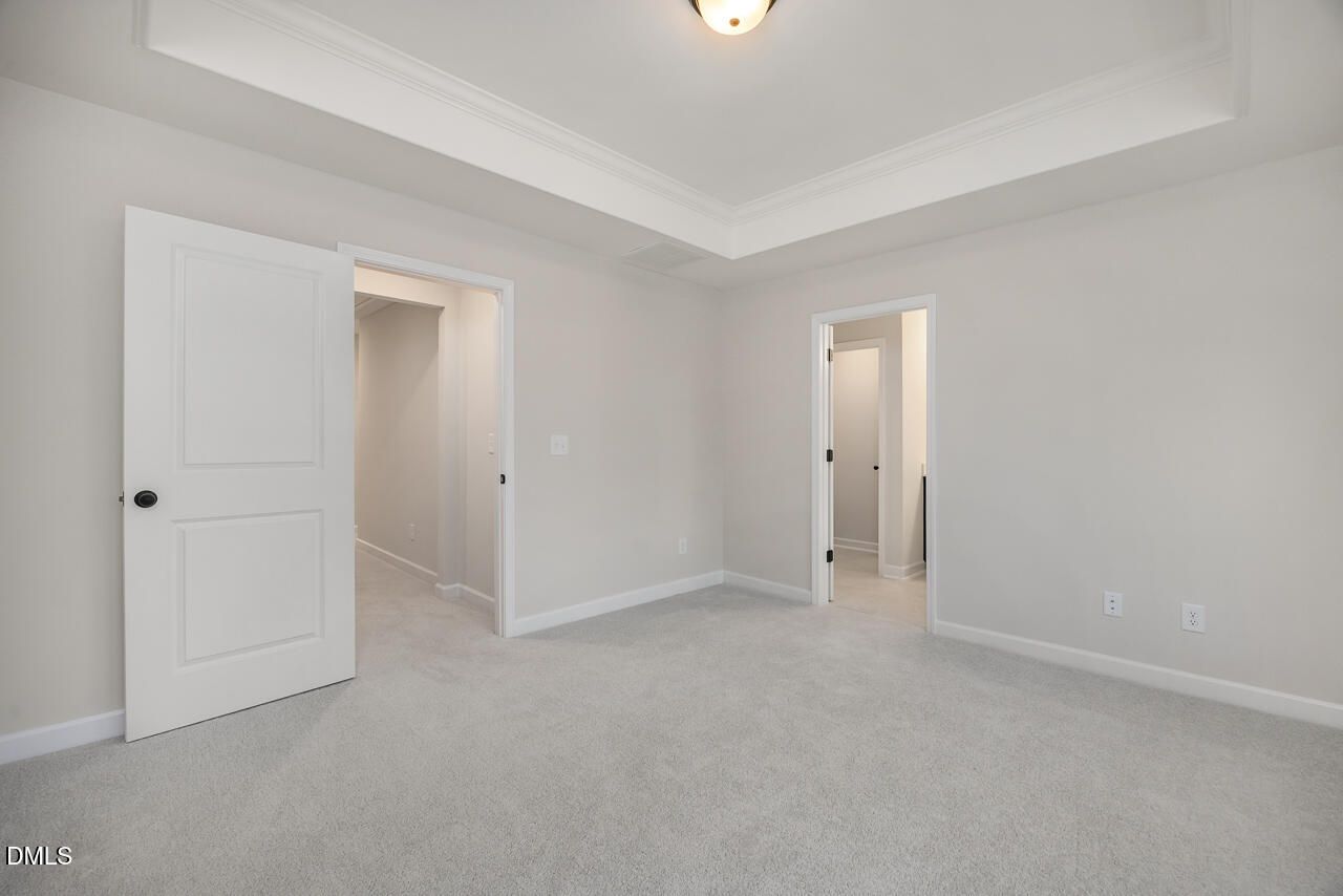 Spacious bedroom with light gray walls, gray carpet, tray ceiling, and doors to closet and bath in Davidson Homes The Mitchell, Knightdale NC