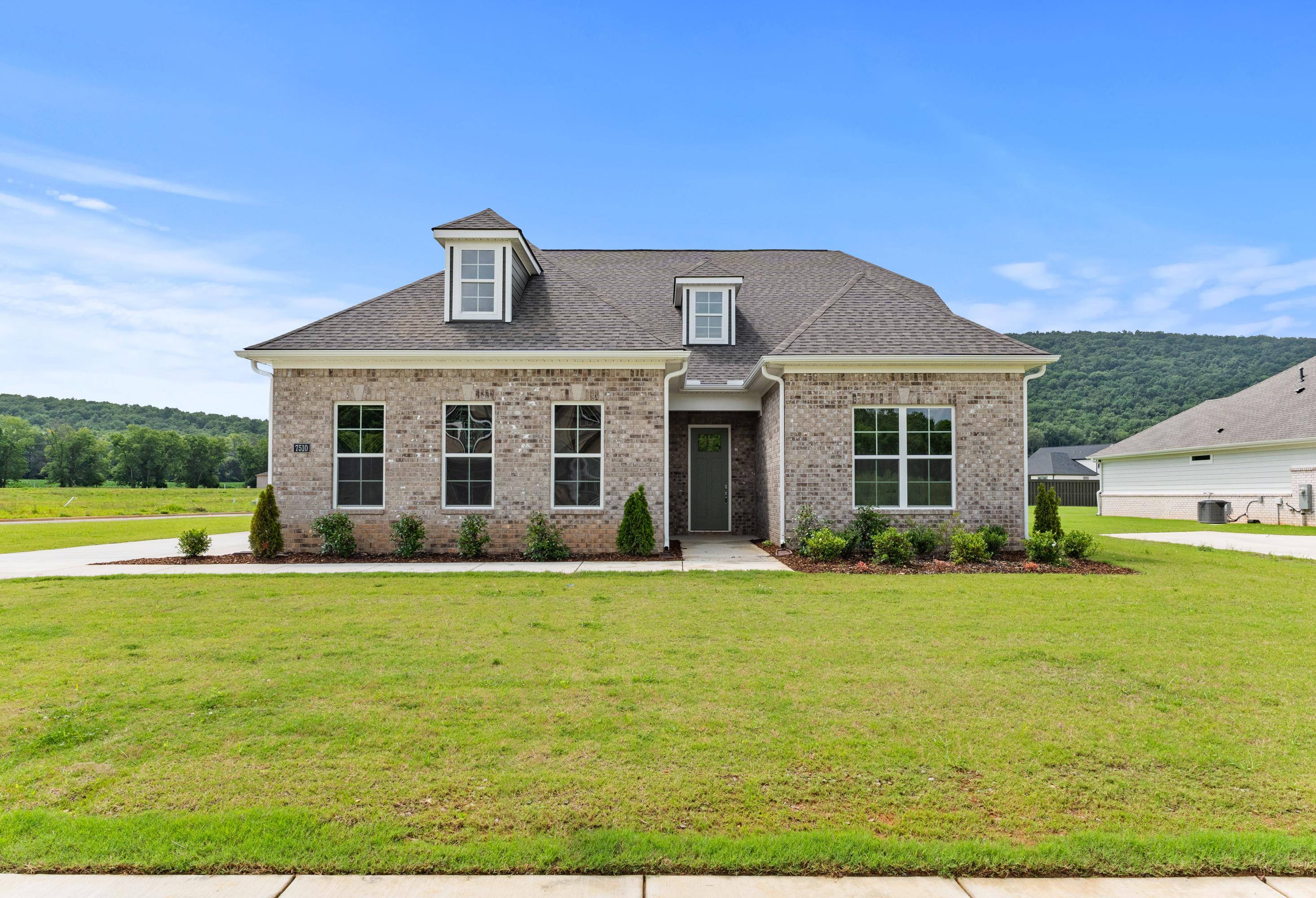 Brick exterior of The Oxford A 2-story home by Evermore Homes in Owens Cross Roads, Alabama, with dormer window, front porch, and lush green lawn