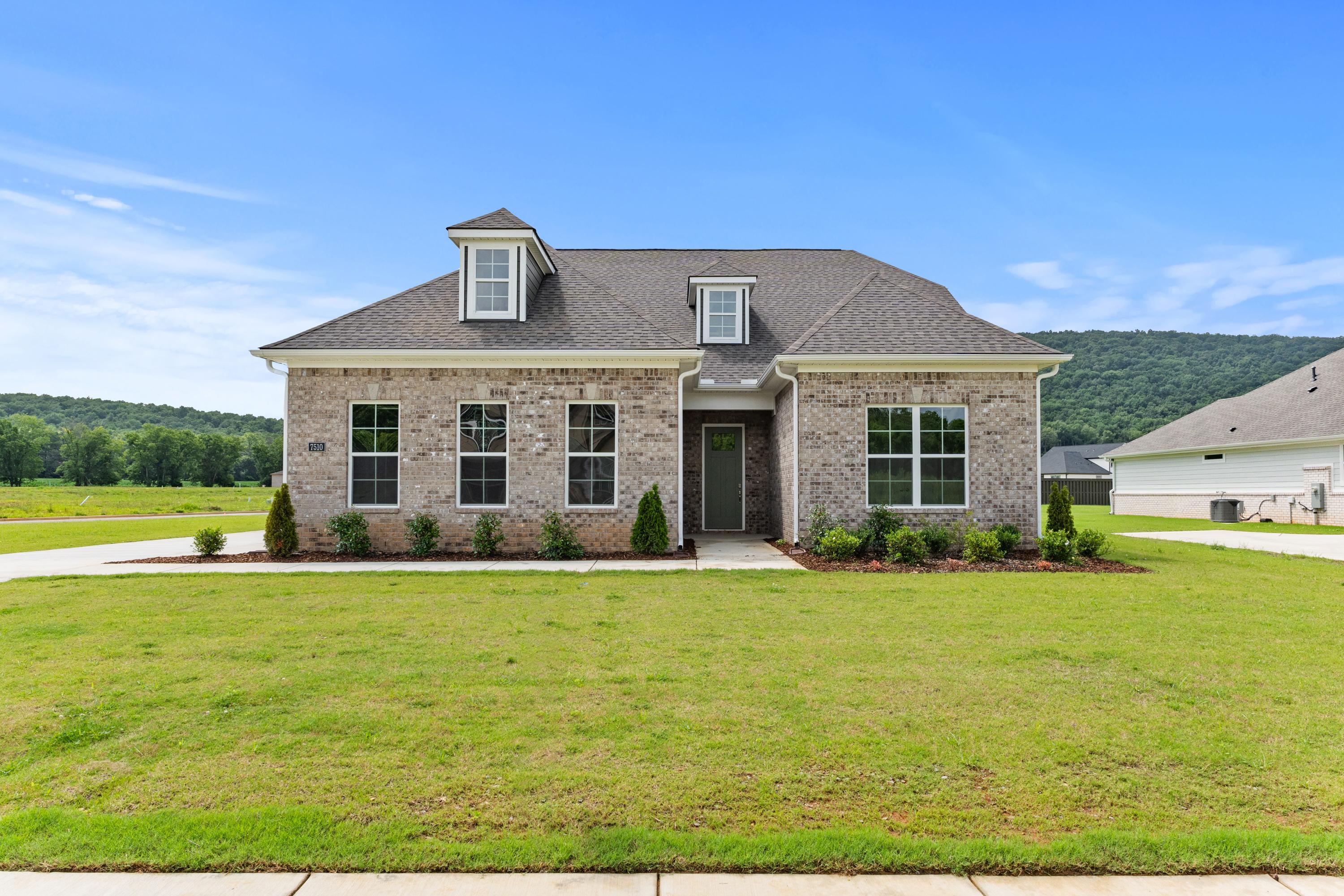 Brick exterior of The Oxford A 2-story home by Evermore Homes in Owens Cross Roads, Alabama, with dormer window, front porch, and lush green lawn