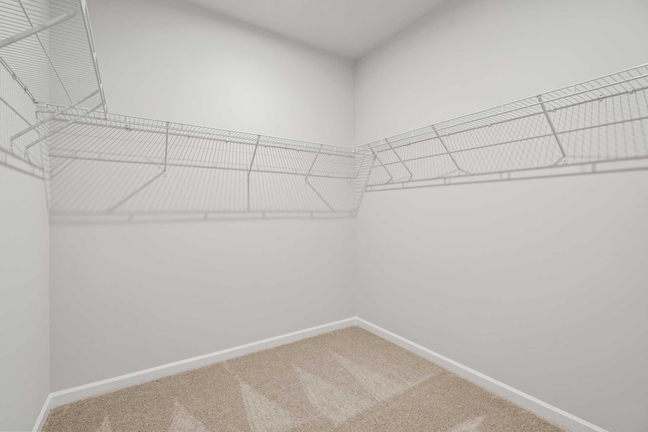 Spacious walk-in closet in The Ash B master suite at Wehunt Meadows featuring wire shelving and beige carpet