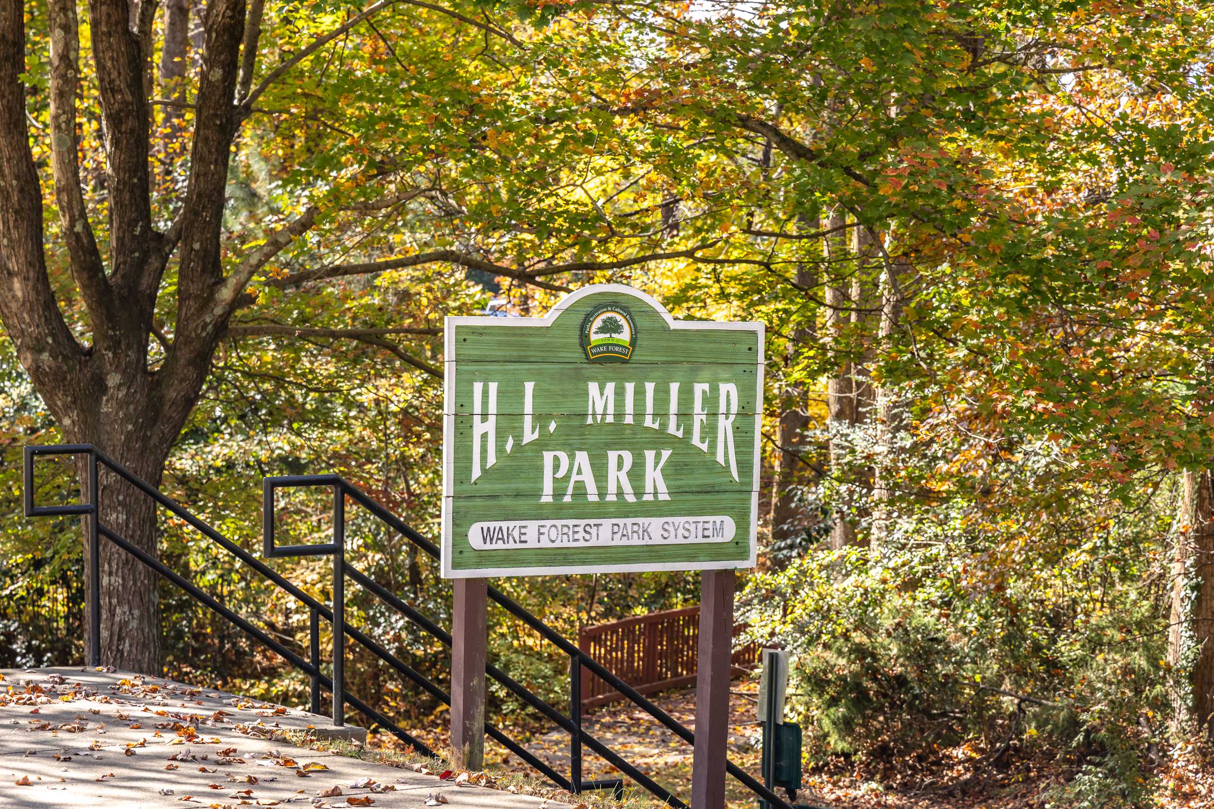 H.L. Miller Park entrance sign in Wake Forest NC amid autumn trees and wooden stairs with black railings