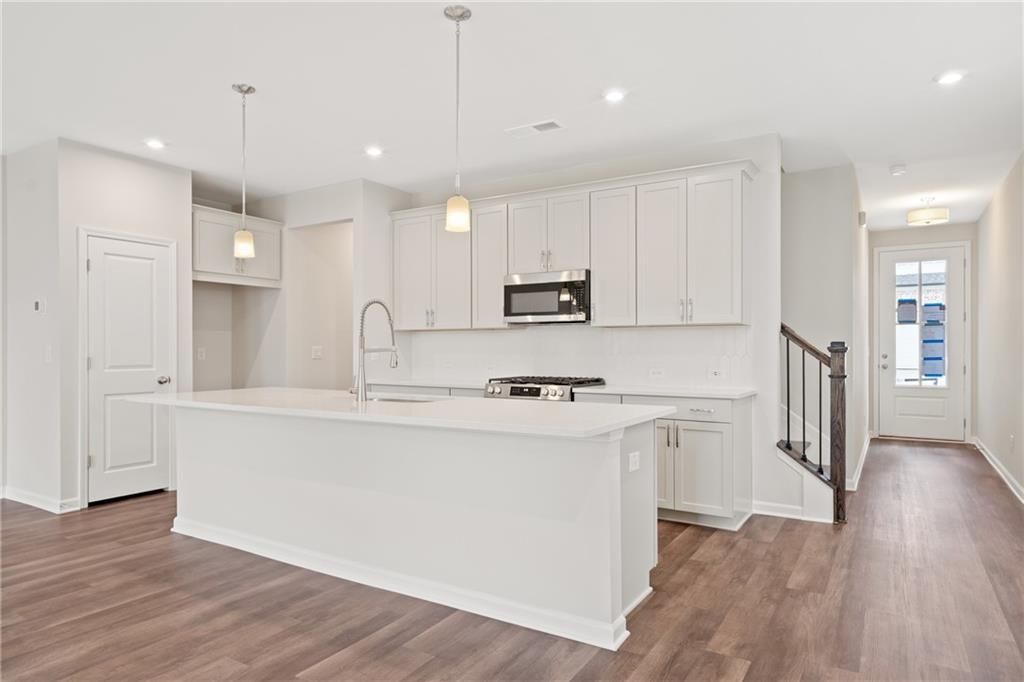 Modern white kitchen with large island, stainless appliances, and hardwood floors in The Cary B by Davidson Homes, Kennesaw, GA