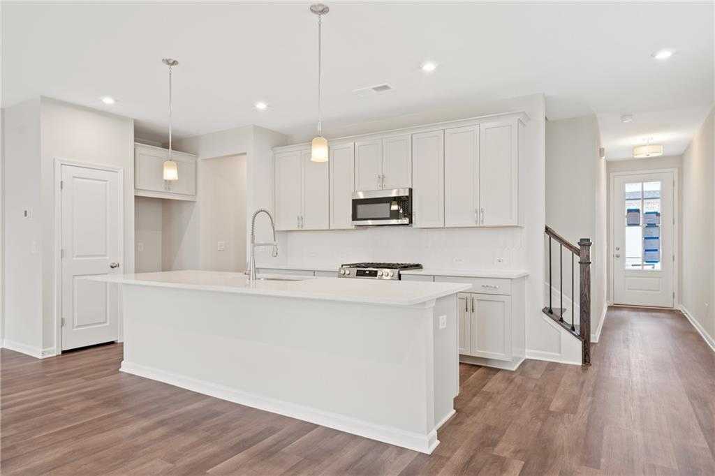 Modern white kitchen with large island, stainless appliances, and hardwood floors in The Cary B by Davidson Homes, Kennesaw, GA