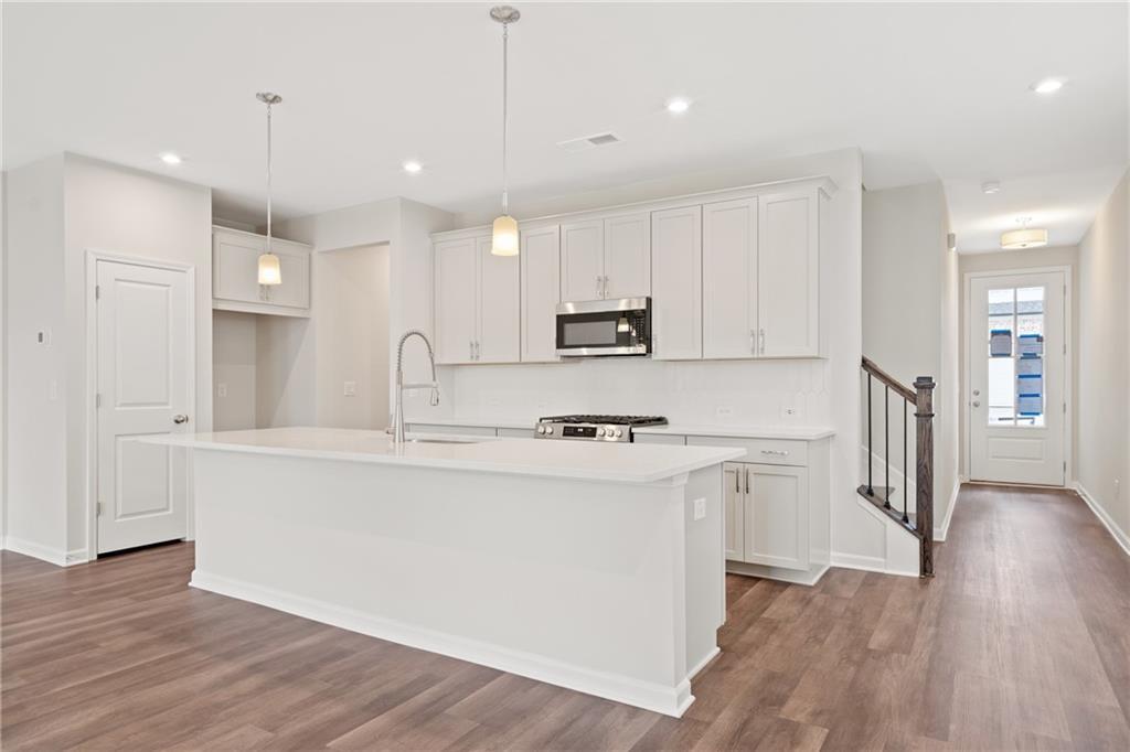 Modern white kitchen with large island, stainless appliances, and hardwood floors in The Cary B by Davidson Homes, Kennesaw, GA