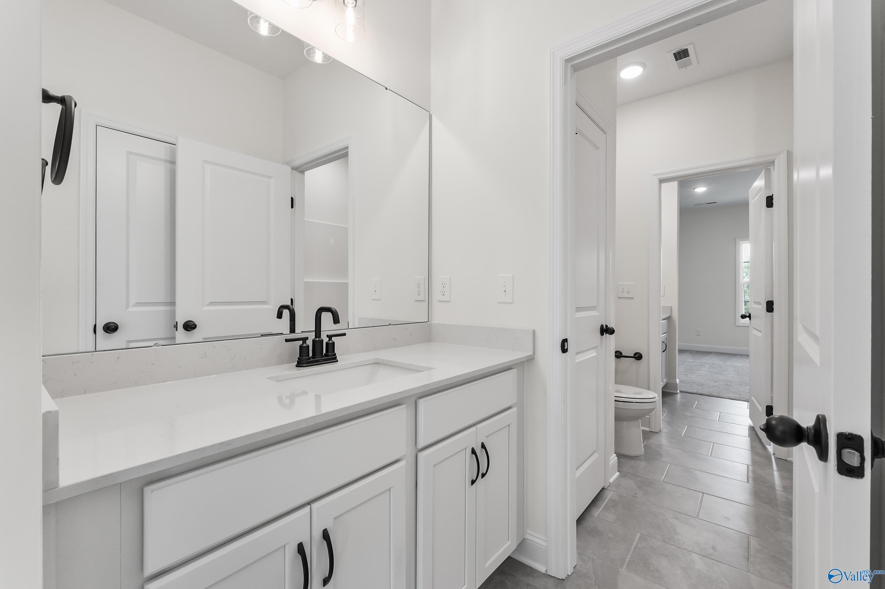 Elegant white powder room with quartz vanity, black faucet, and open door to bedroom in Davidson Homes The Finleigh, Harvest, AL