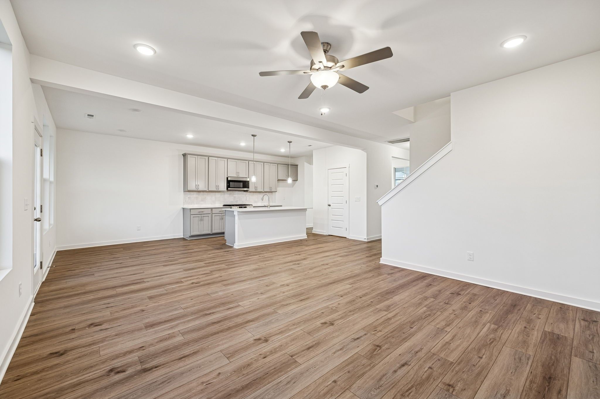 Open-concept kitchen and living space with white cabinets, wood floors, island sink, and ceiling fan in Davidson Homes The Willow, Calista Farms
