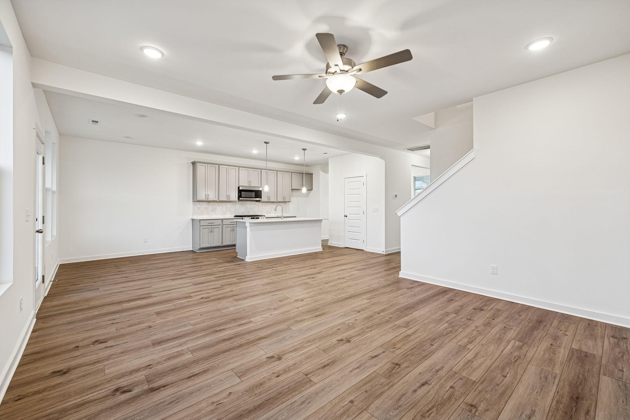Open-concept kitchen and living space with white cabinets, wood floors, island sink, and ceiling fan in Davidson Homes The Willow, Calista Farms