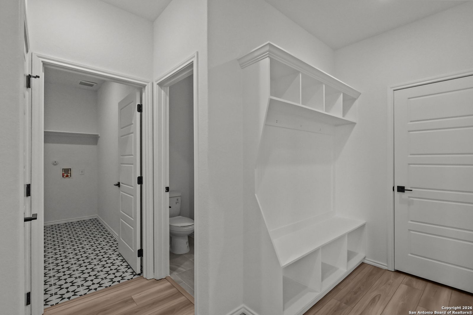 Bright mudroom with white built-in bench, open shelves, and adjacent powder bath in Davidson Homes The Douglas E, San Antonio