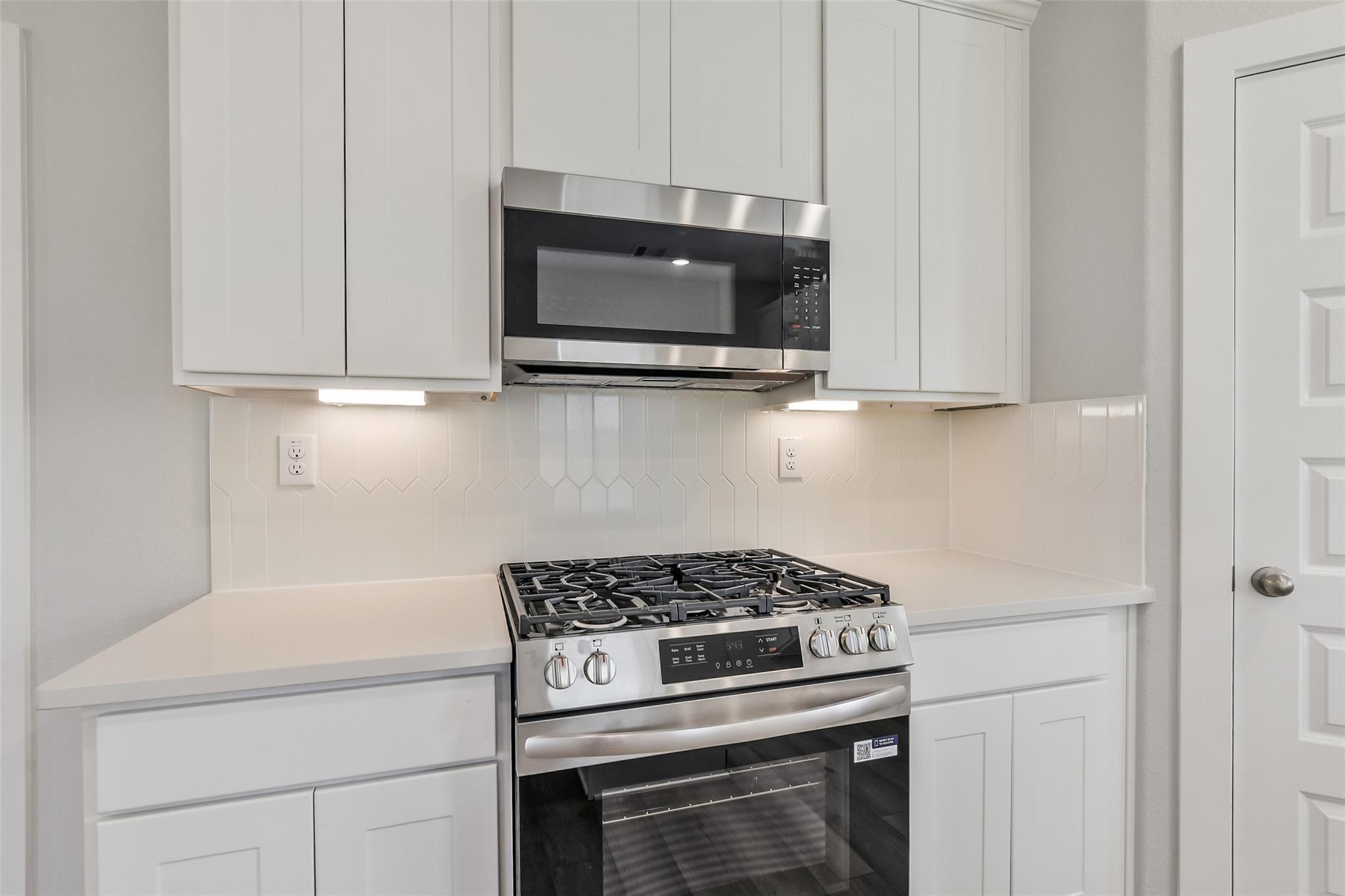 Modern white kitchen with shaker cabinets, stainless gas range, microwave, and subway tile backsplash in Davidson Homes The Trinity F, Magnolia, TX