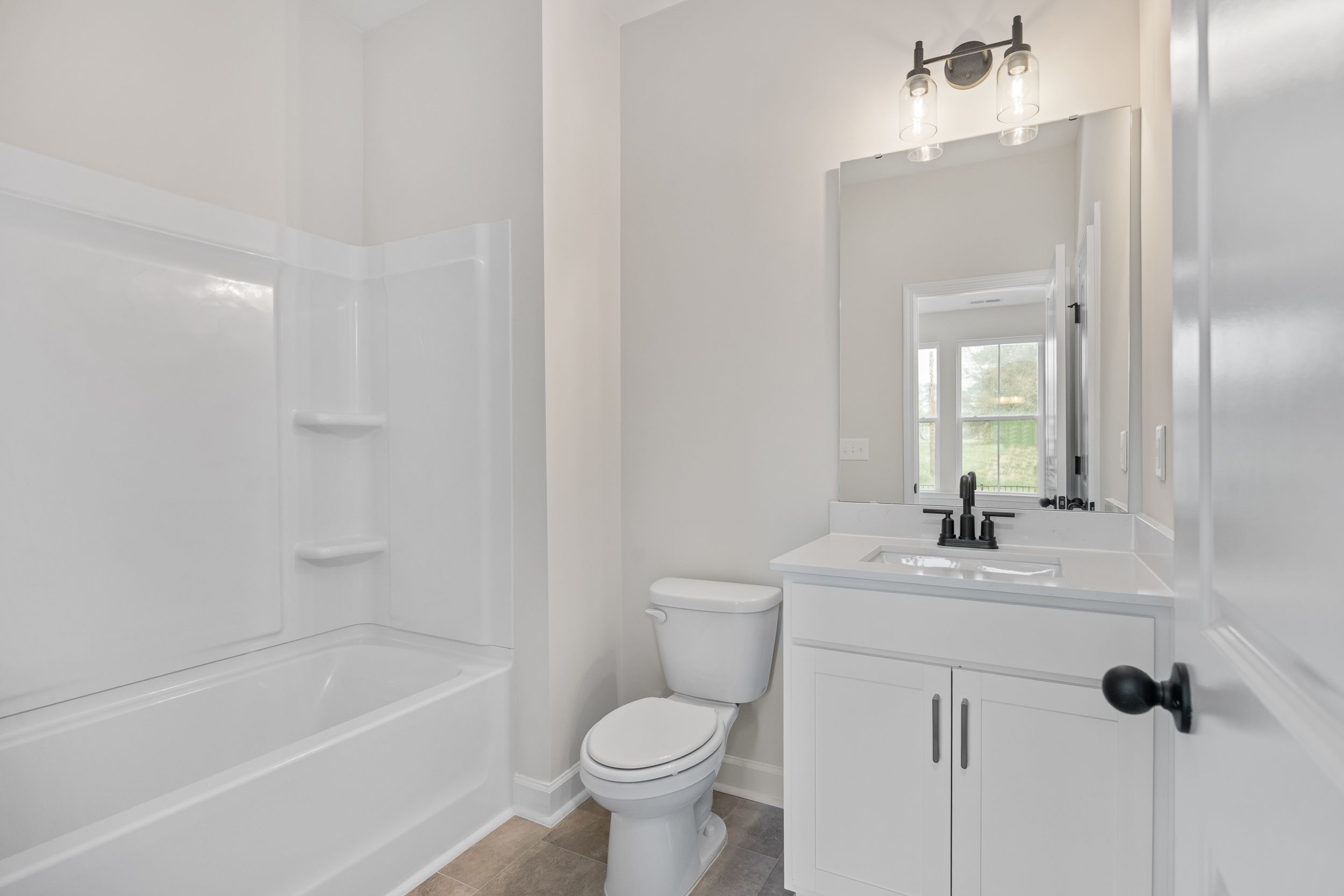 Modern white bathroom with tiled shower, soaking tub, vanity sink, toilet, and mirror in Forestville Yard Townhomes, Knightdale NC