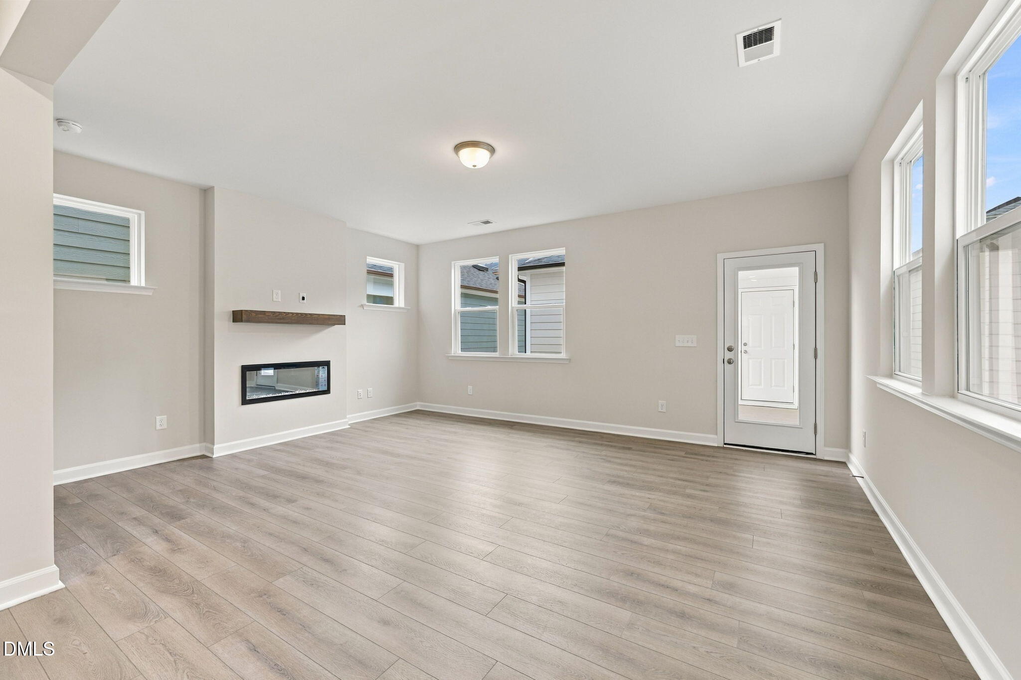 Bright open-concept living room with luxury vinyl plank flooring, linear fireplace, and glass-panel door in Davidson Homes' The Alexander B, Knightdale, NC.