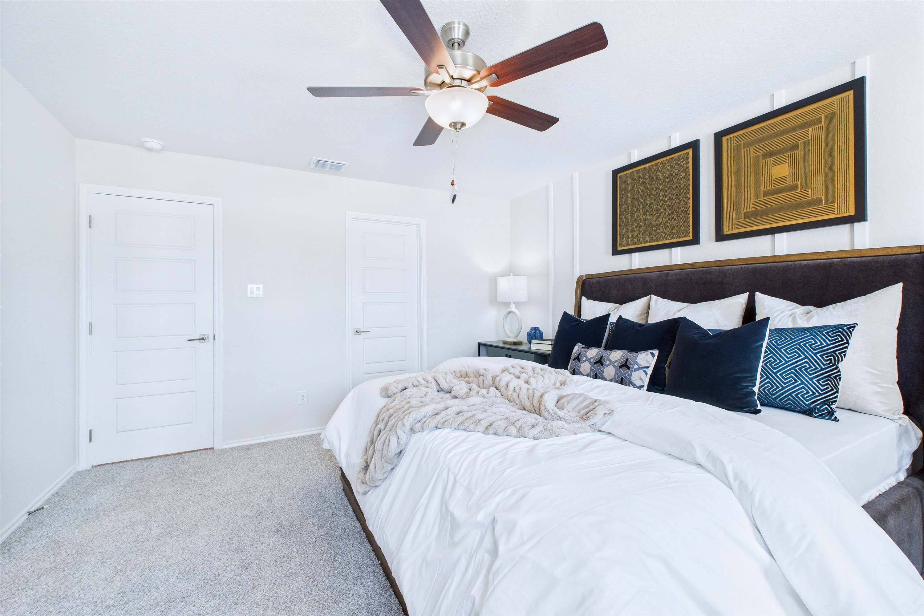 Spacious master bedroom in The Gillian C featuring a plush bed, modern ceiling fan, and elegant wall decor.