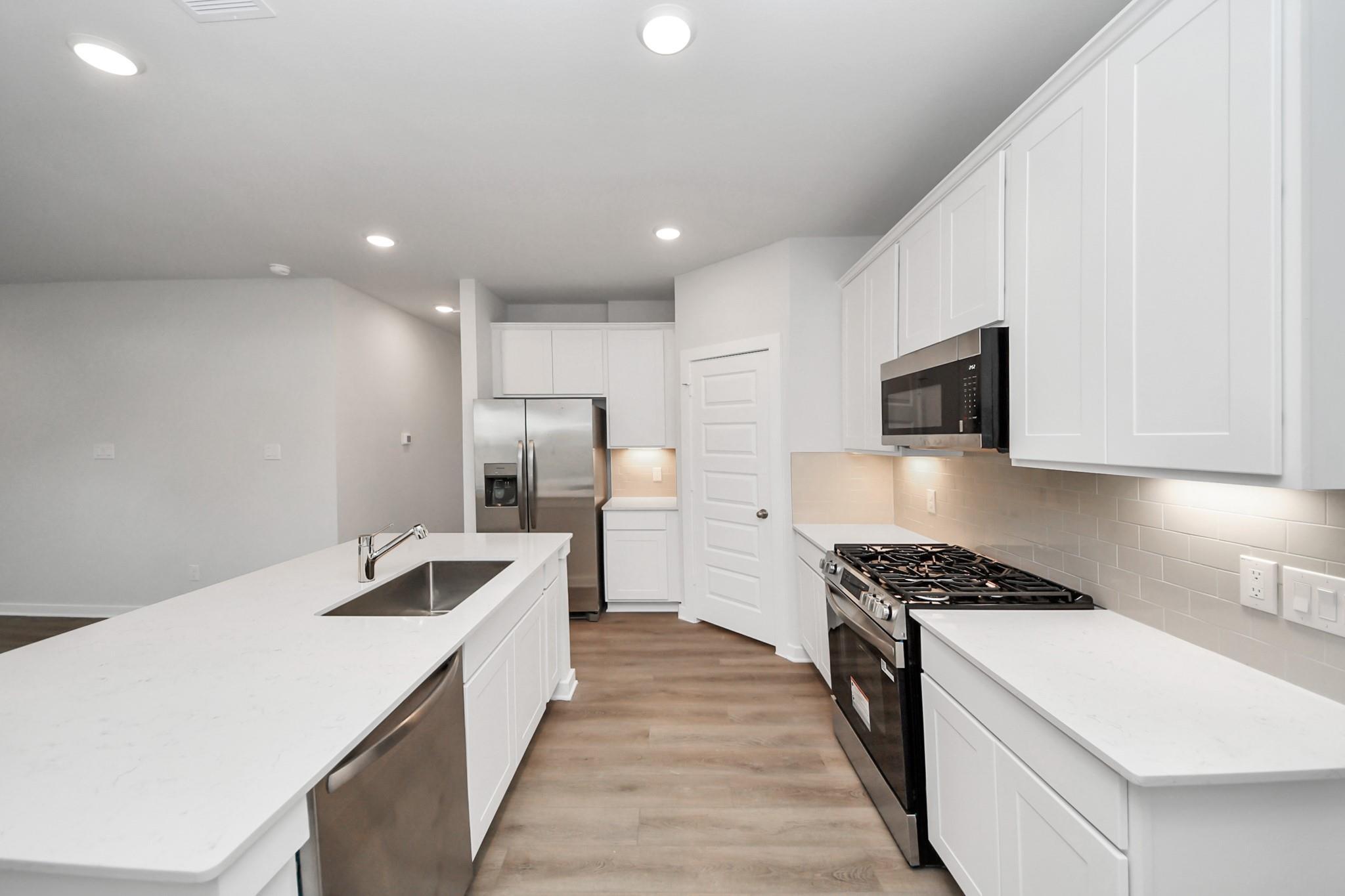 Bright kitchen with white shaker cabinets, quartz island, stainless appliances, and gas range in The Sabine F, Conroe, Texas