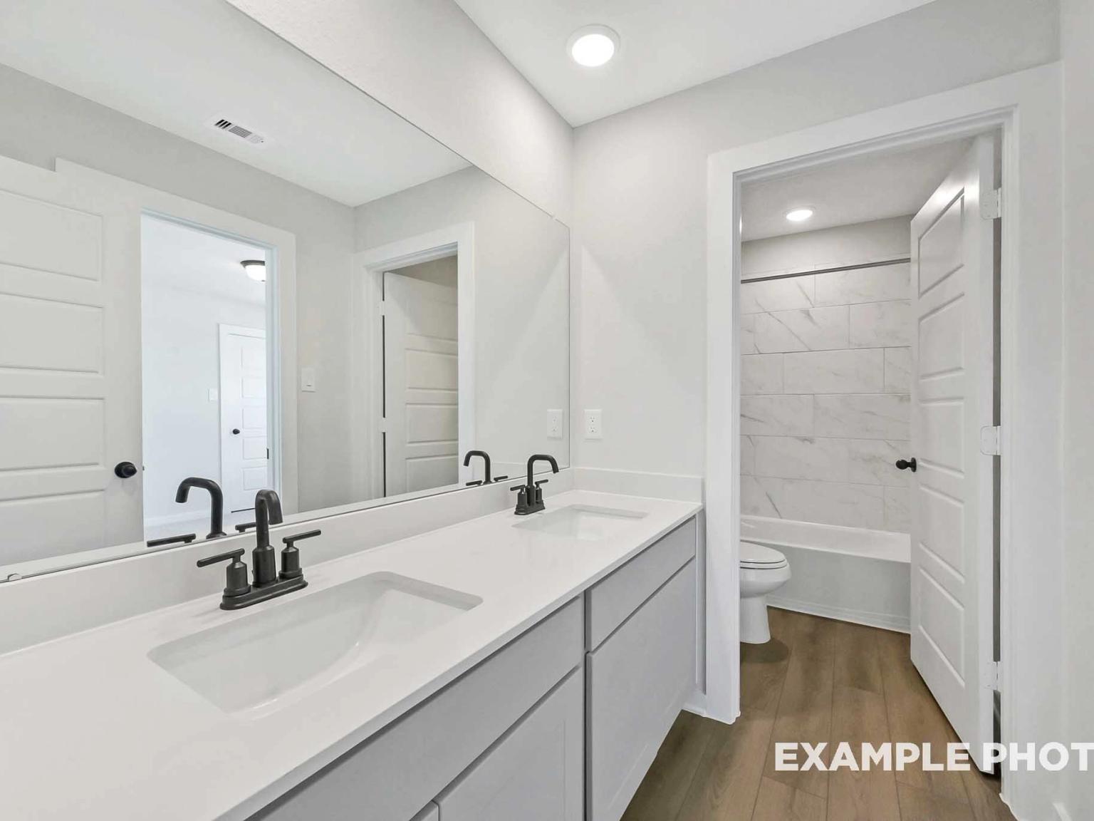 Modern bathroom with double vanity, marble-style tub surround, and matte black fixtures in The Sequoia C, Crosby, Texas.