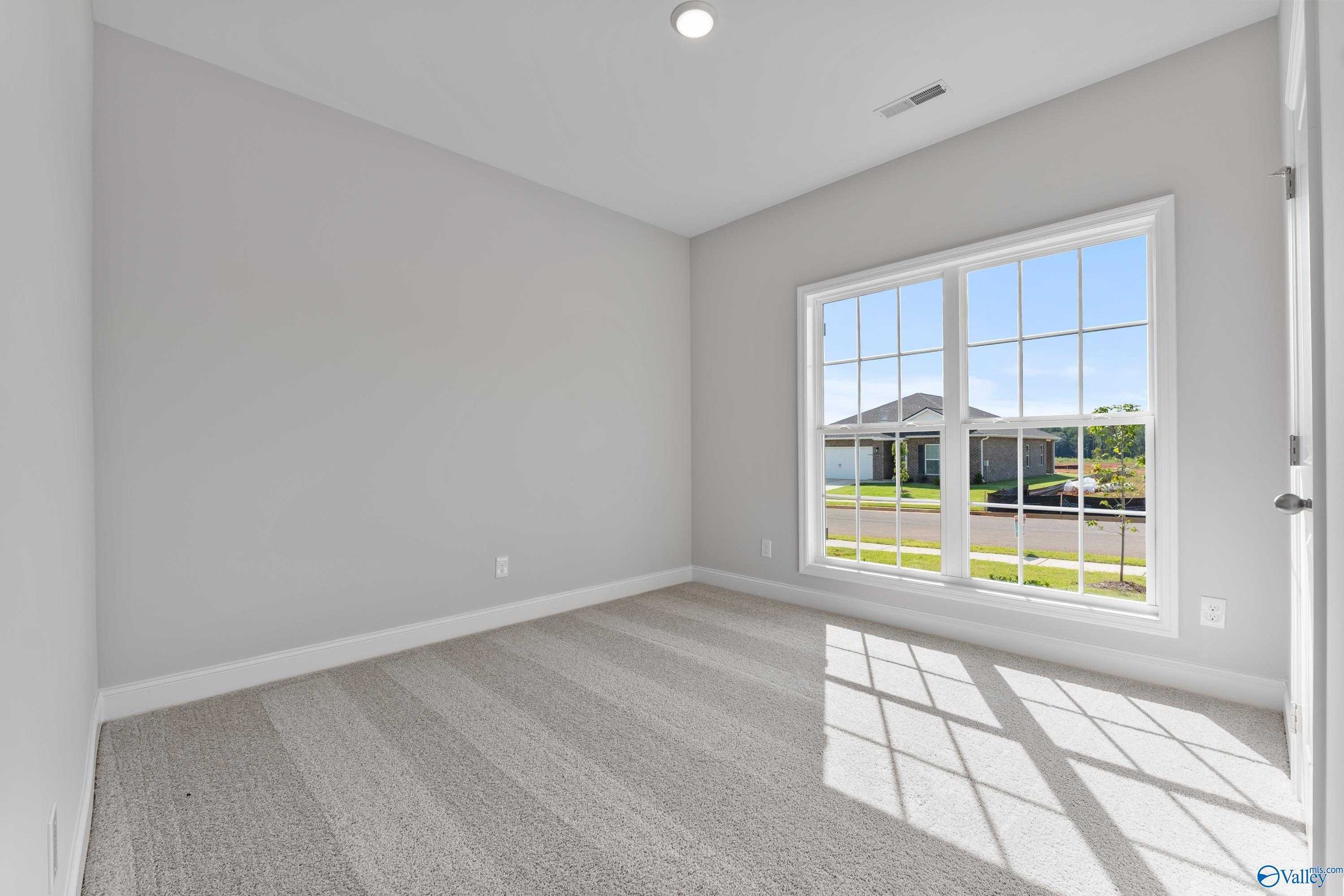 Bright secondary bedroom with gray walls, striped carpet, and large window view of neighborhood in Davidson Homes The Franklin C, Toney, Alabama