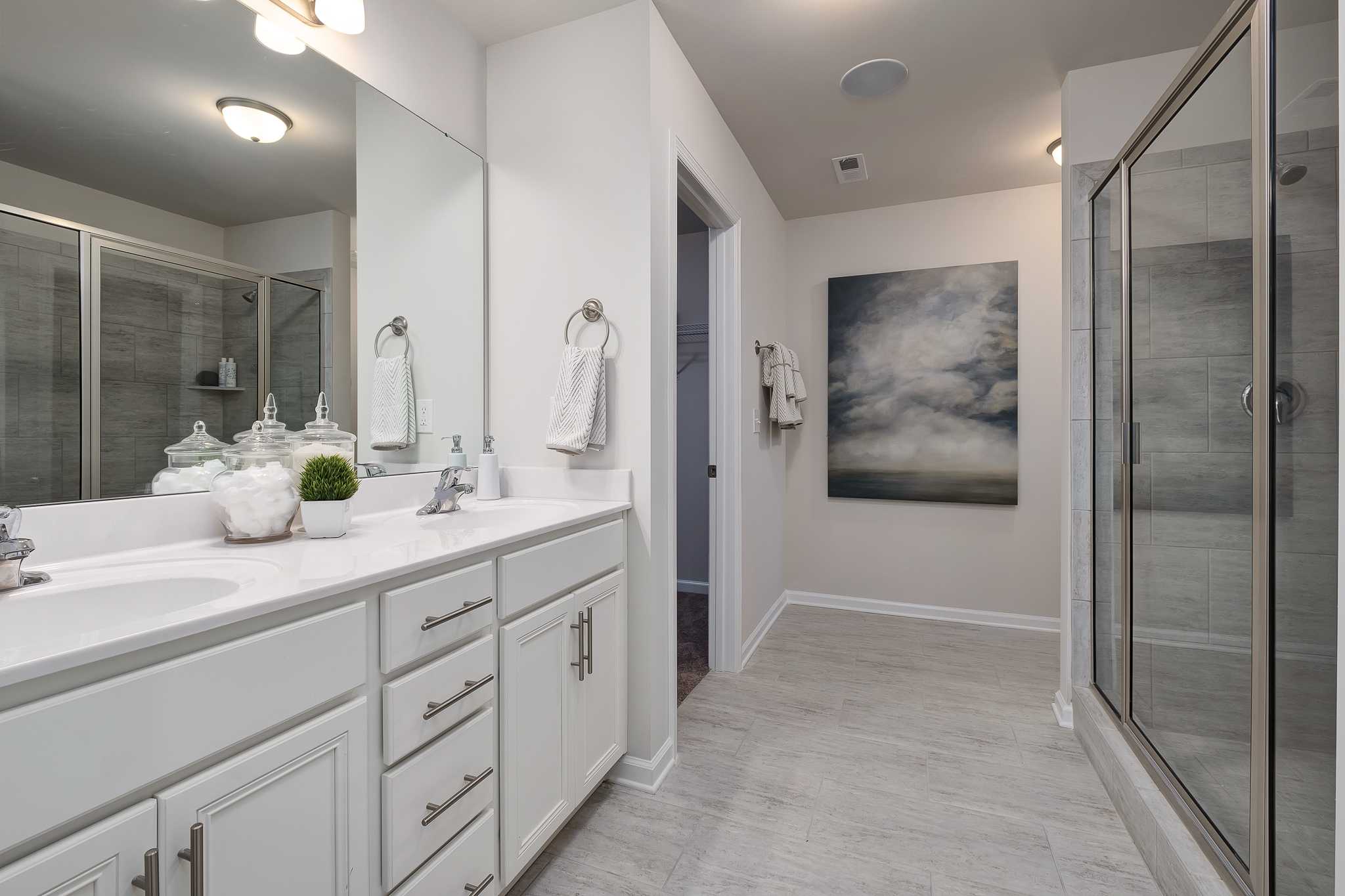 Spacious primary bathroom at The Reserve at Overton in Hampton Cove AL with white double vanity, glass shower, and abstract wall art