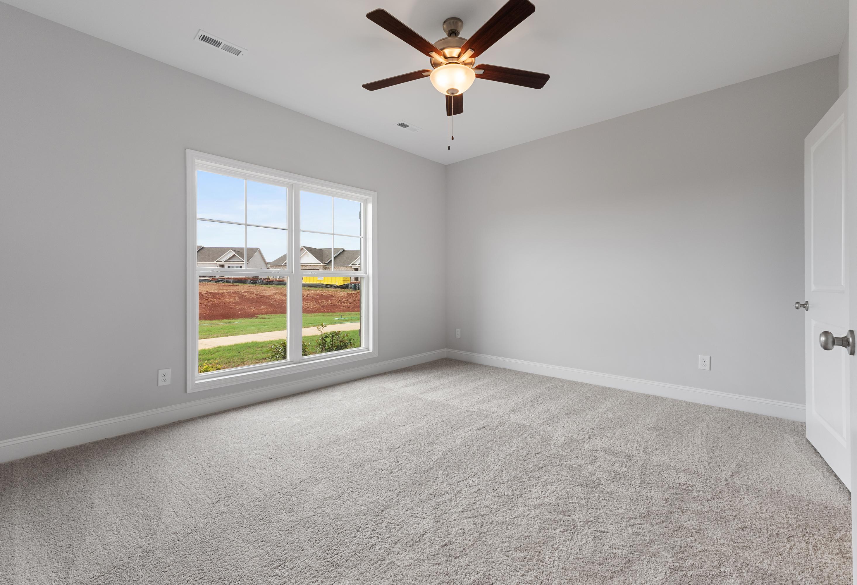 Spacious bedroom in The Copeland B with light gray walls, large window overlooking lawn, ceiling fan, neutral carpet