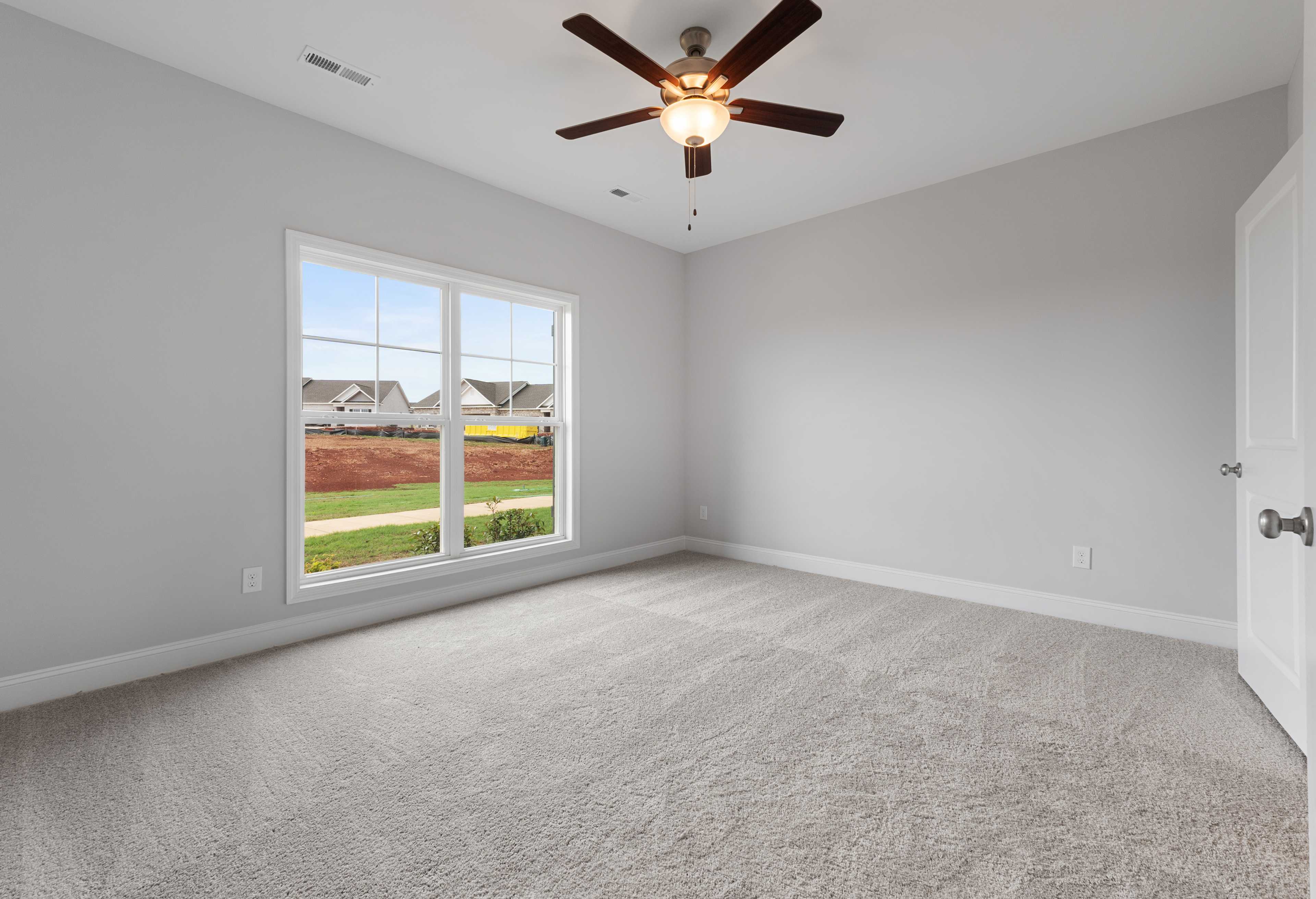 Spacious bedroom in The Copeland B with light gray walls, large window overlooking lawn, ceiling fan, neutral carpet