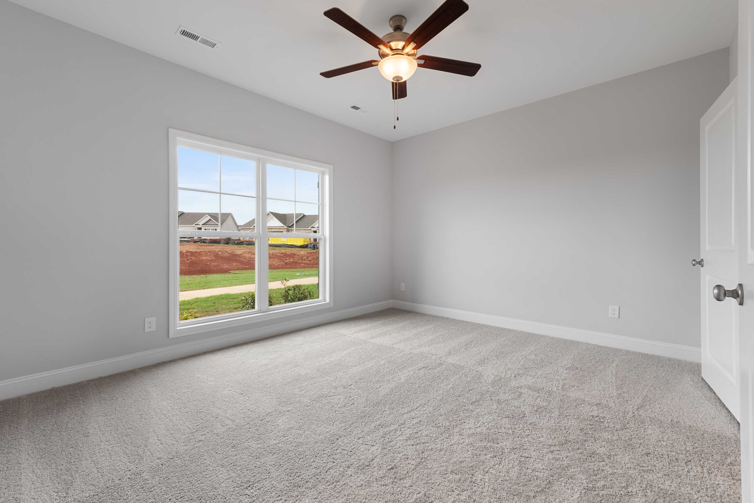 Spacious bedroom in The Copeland B with light gray walls, large window overlooking lawn, ceiling fan, neutral carpet