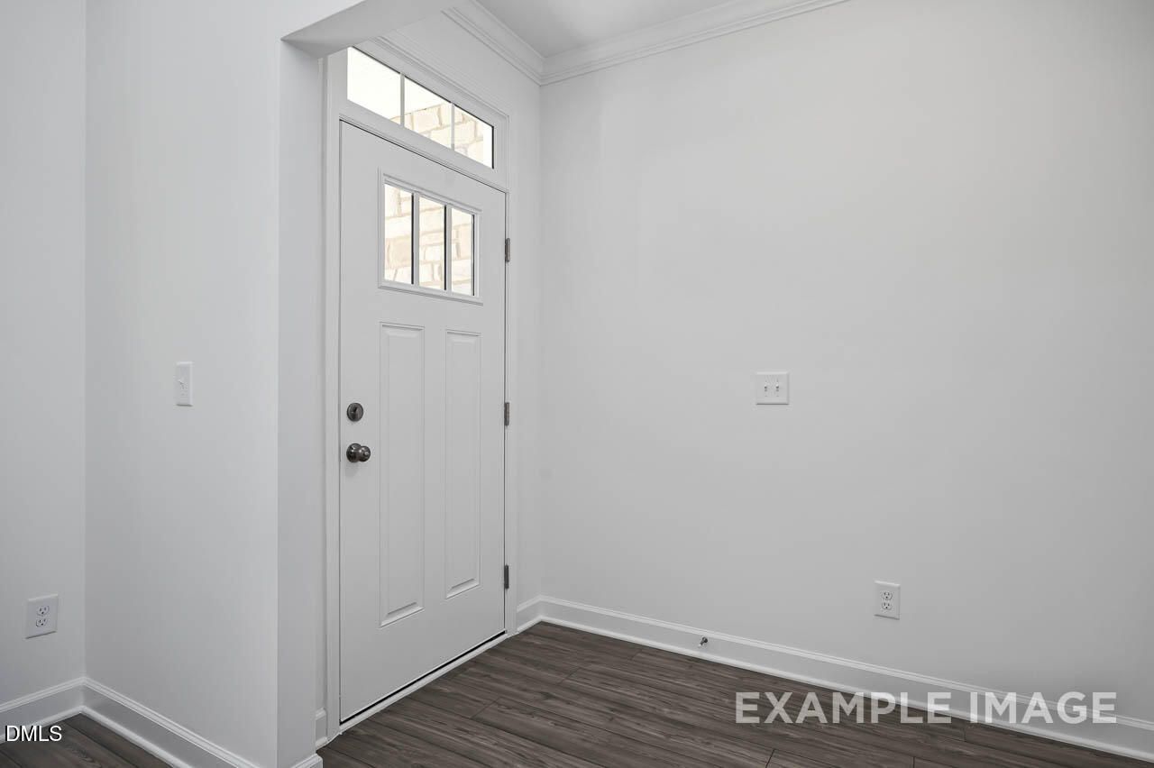 Bright entryway with white paneled front door, glass transom, and hardwood floors in Davidson Homes The Willow D, Zebulon, NC