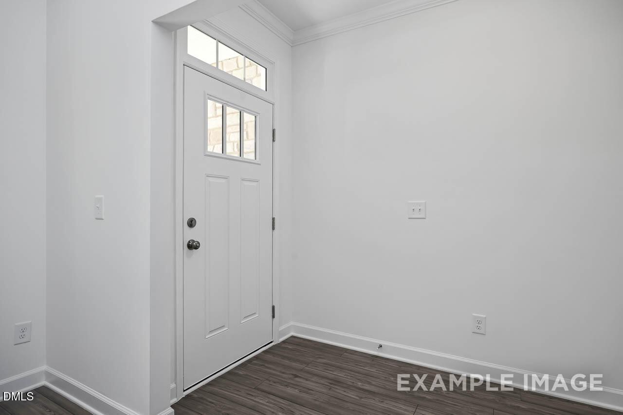Bright entry foyer with white paneled door, transom window, and hardwood floors in The Willow D home, Zebulon, NC