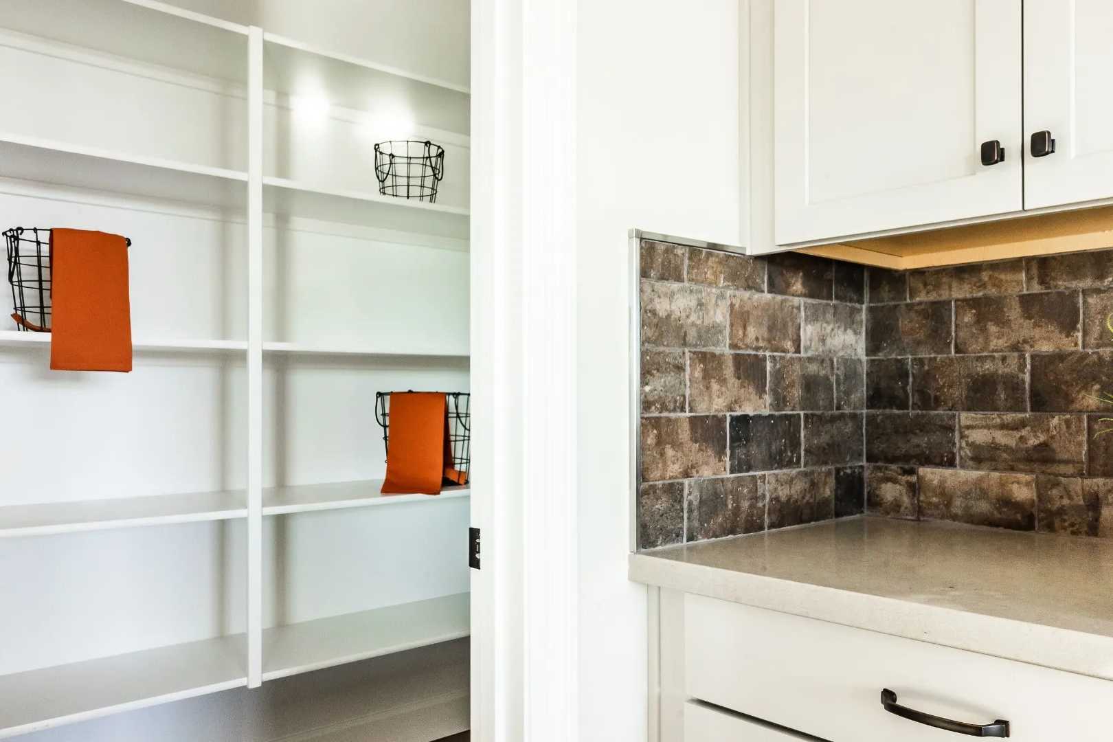 Spacious walk-in pantry with white shelves and orange towel baskets in Westwood home by Davidson Homes, Prescott AZ, adjacent to white kitchen cabinets and subway tile backsplash