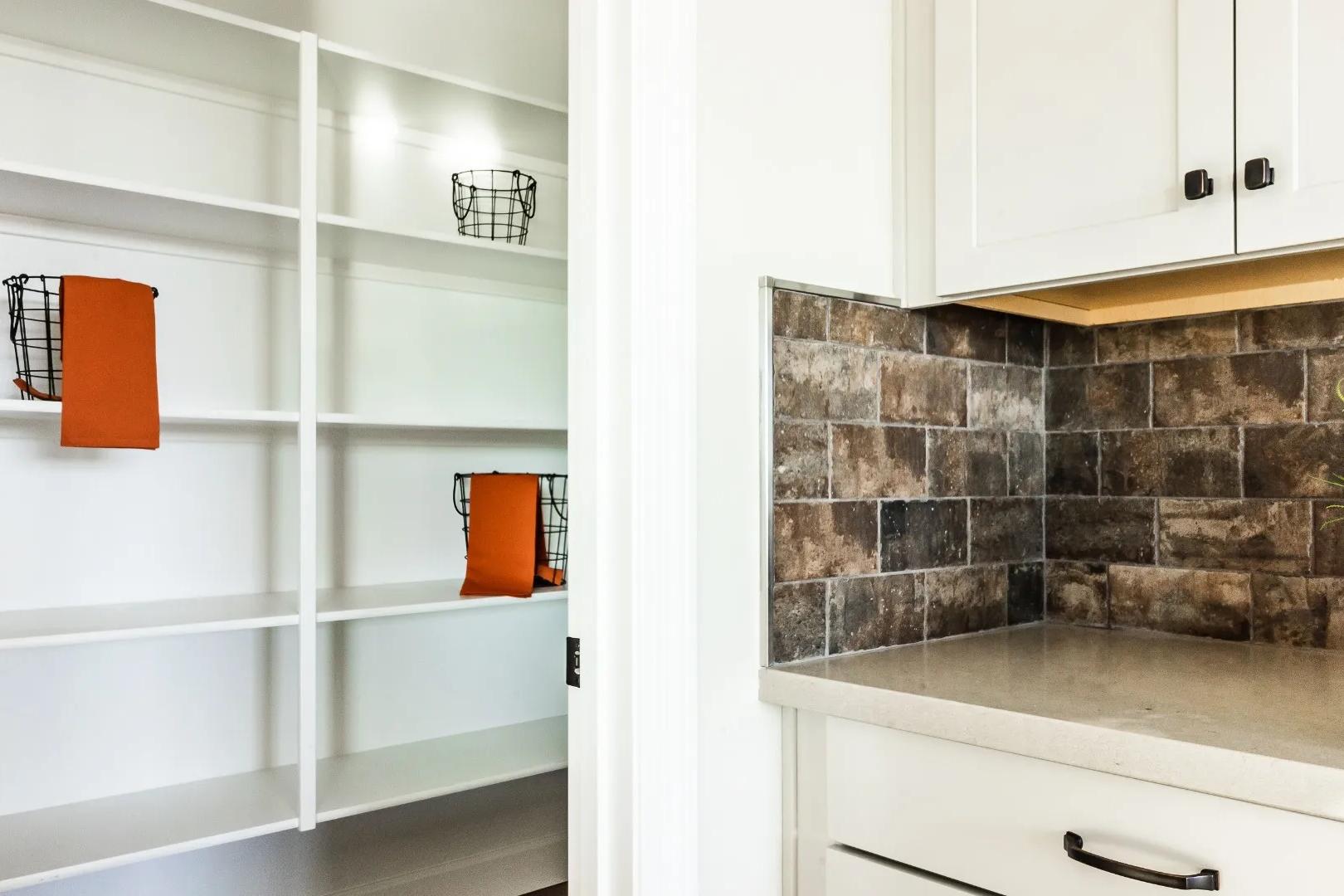 Spacious walk-in pantry with white shelves and orange towel baskets in Westwood home by Davidson Homes, Prescott AZ, adjacent to white kitchen cabinets and subway tile backsplash