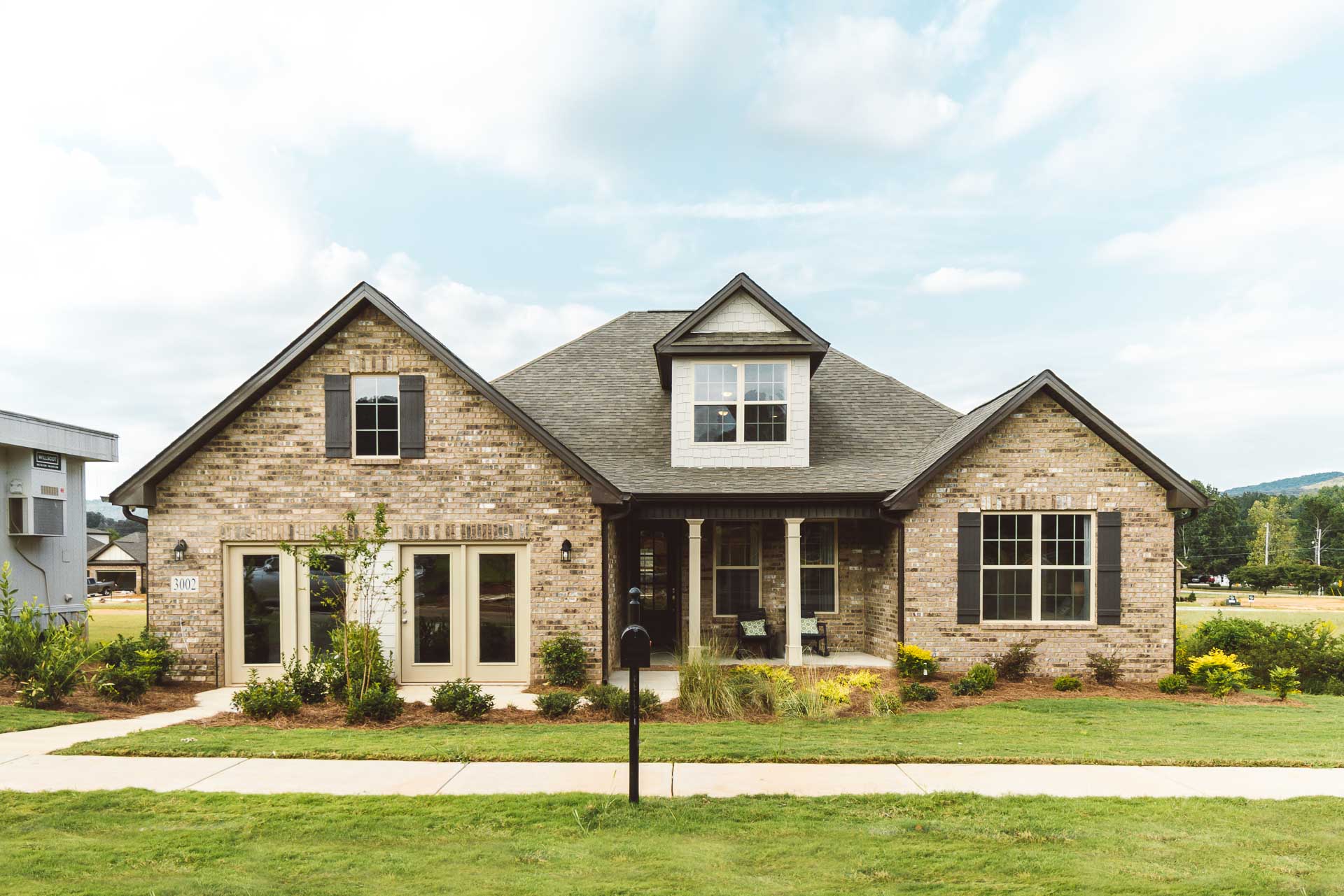 Brick Craftsman home exterior at Chimney Creek in Hampton Cove, Alabama with covered porch, brick facade, and lush landscaping