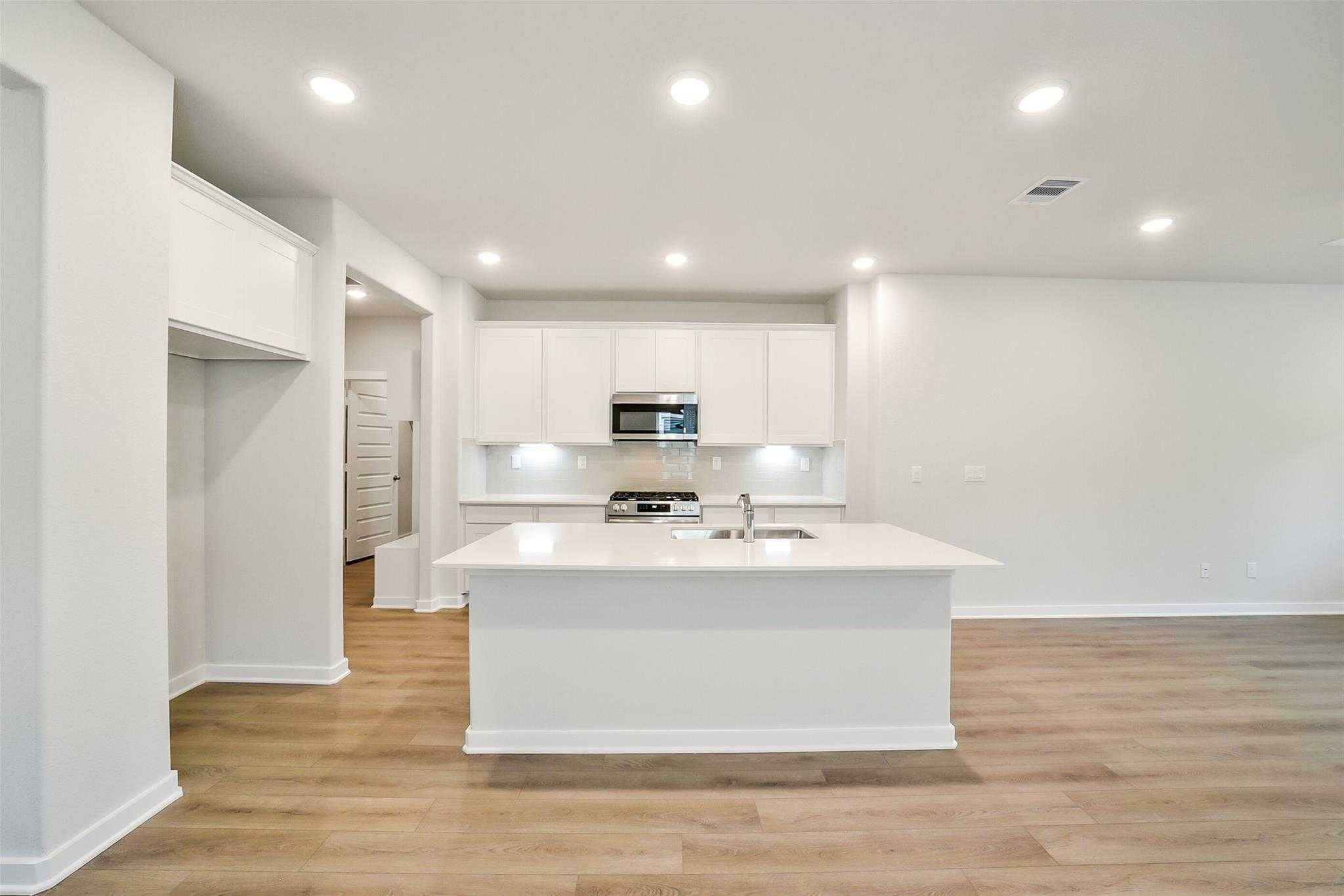 Modern white kitchen featuring large island sink, stainless steel appliances, and open layout in The Blanco E by Davidson Homes, Magnolia, Texas