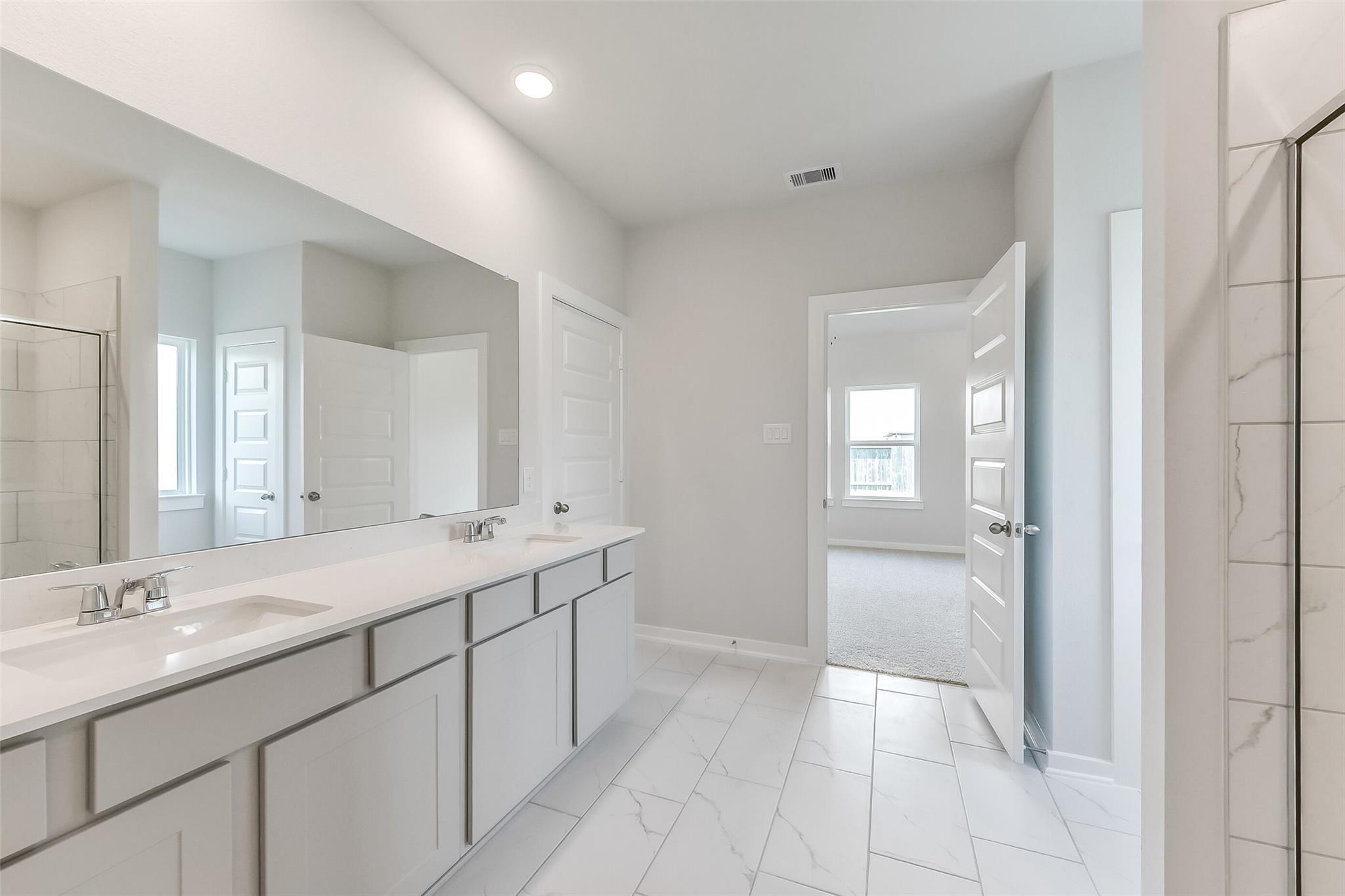 Modern master bathroom featuring double white quartz vanity, subway tile shower, and porcelain tile floor in Davidson Homes The Tierra C, Dayton Texas