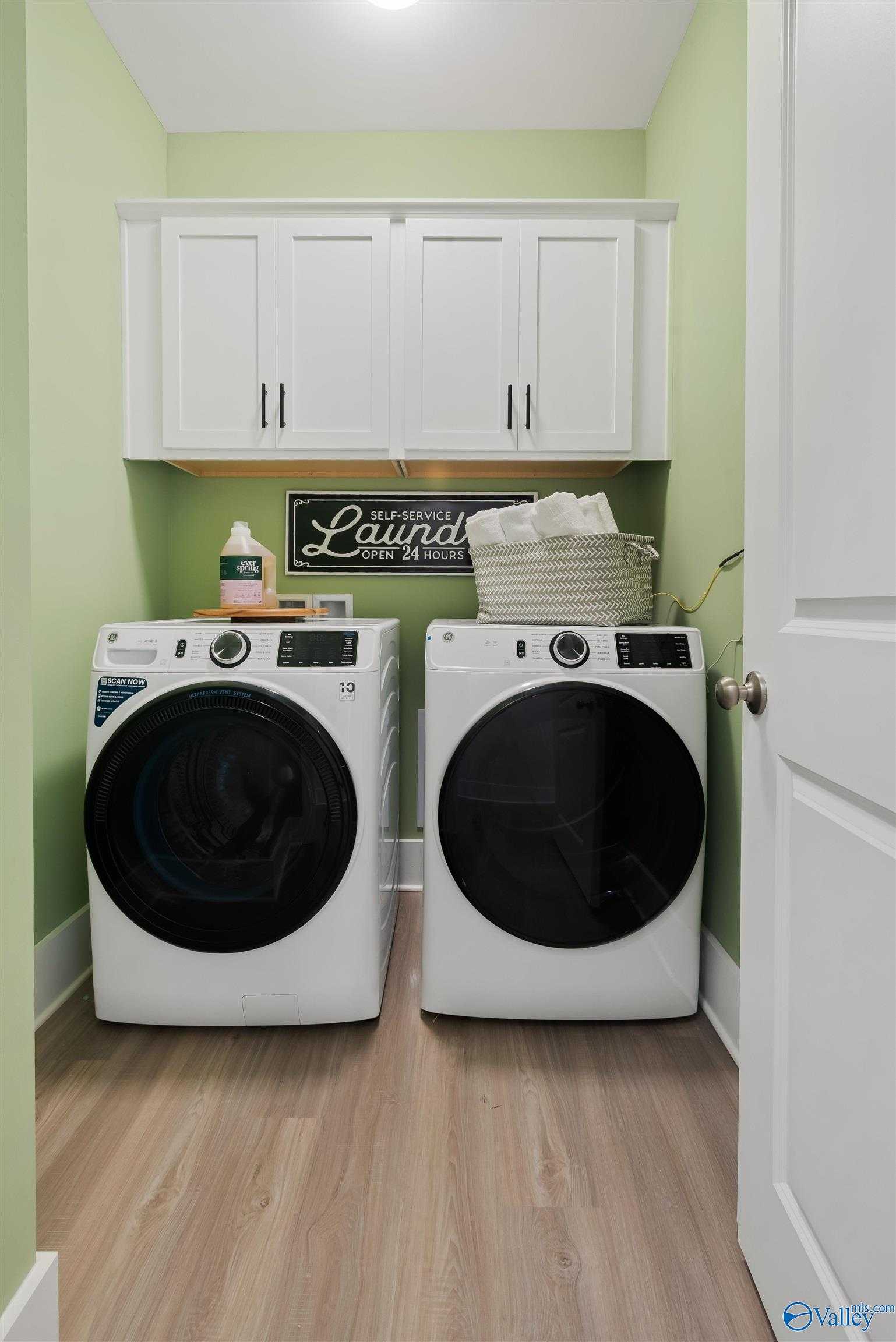 Bright laundry room with white front-load washer, dryer, cabinets on green walls in Davidson Homes The Daphne, Harvest AL