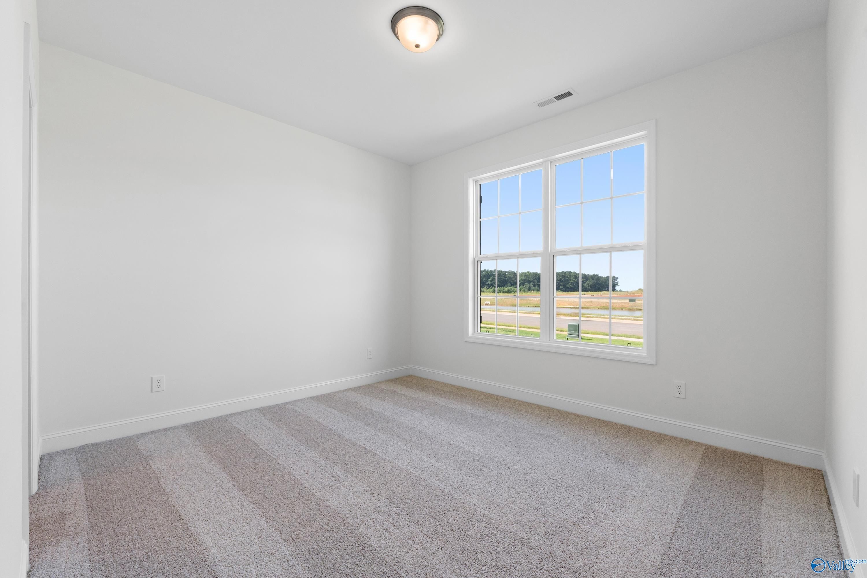 Bright bedroom with large window overlooking fields, white walls, striped carpet in Davidson Homes The Rockford B, Toney, Alabama