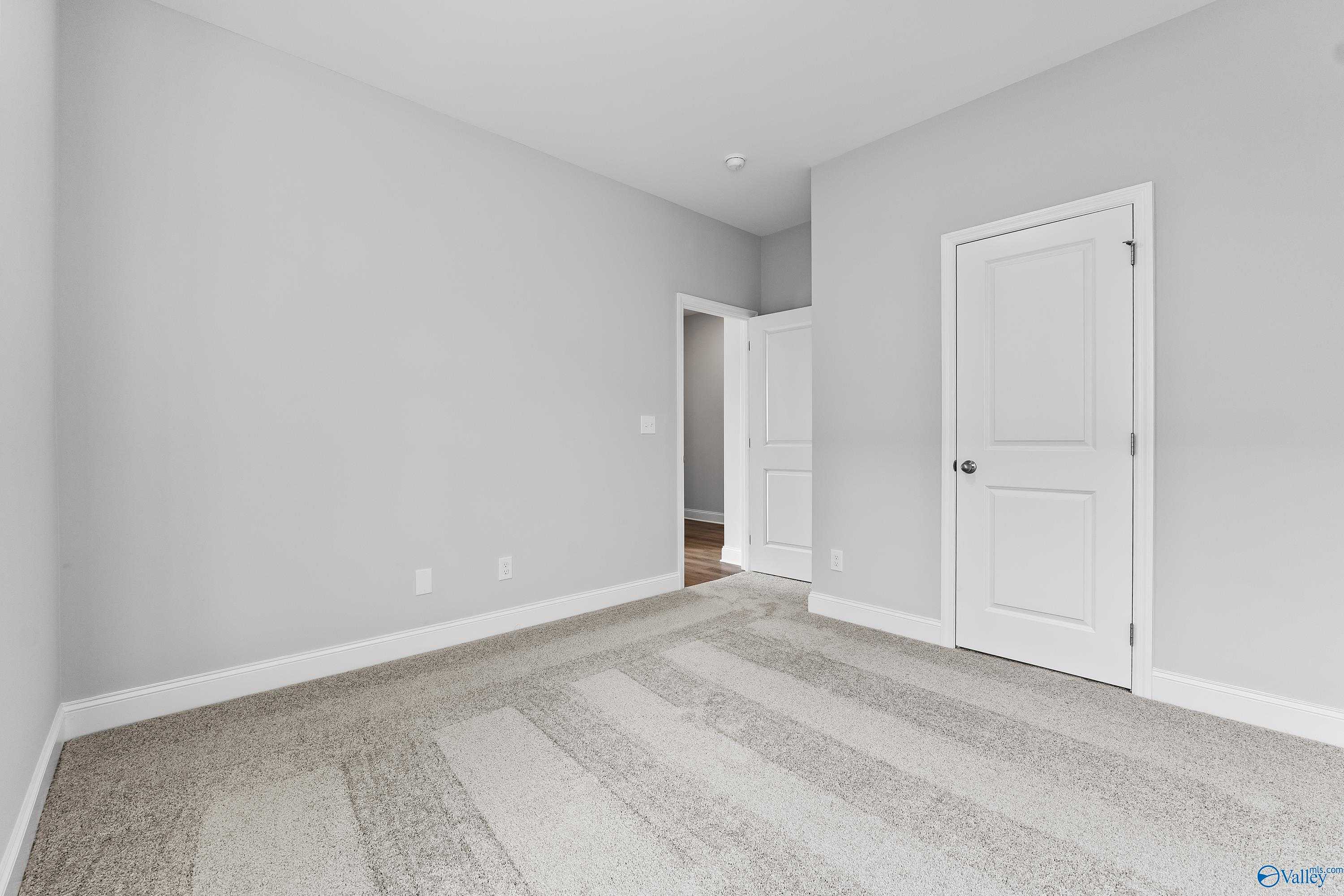 Spacious empty bedroom with light gray walls, white doors, beige carpet in Davidson Homes The Franklin C, Toney, Alabama