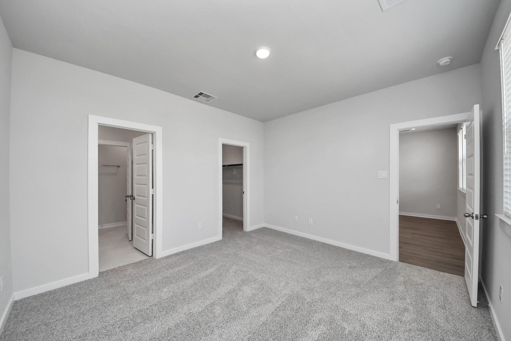 Bright carpeted bedroom with walk-in closets and ensuite access in Davidson Homes The Frio F at Robins Landing, Houston.