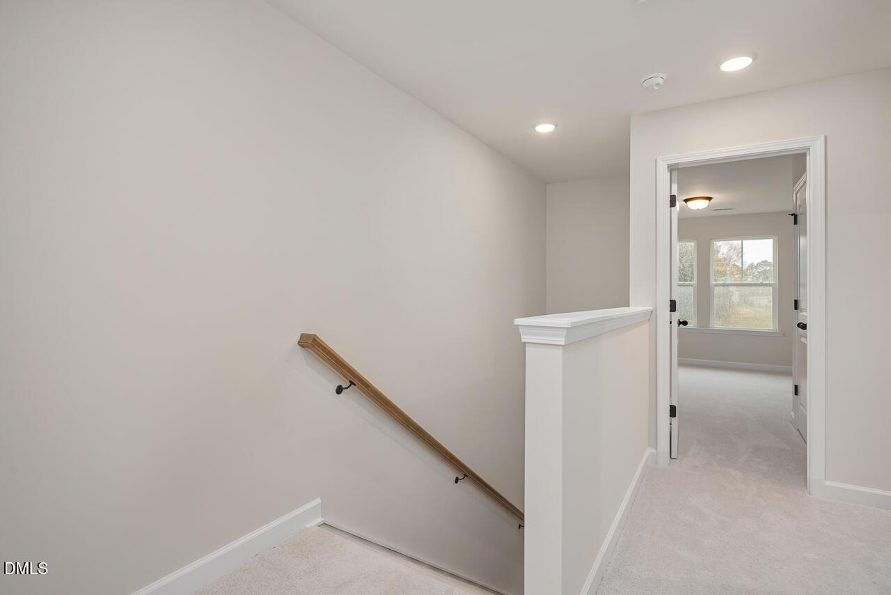 Elegant wooden handrail and white balustrade overlooking carpeted hallway in 4-bedroom The Mitchell home, Knightdale, NC