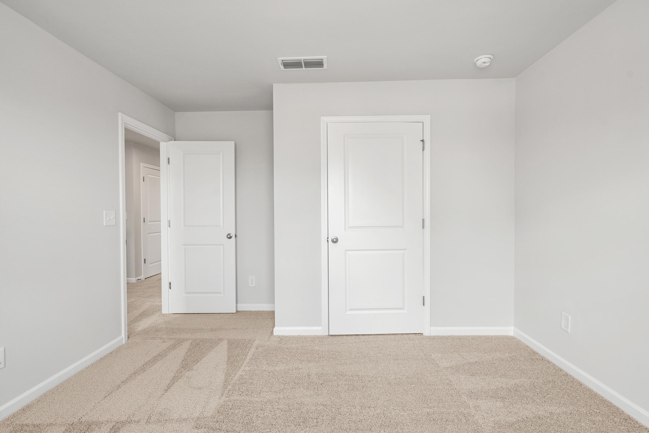 Spacious bedroom in The Ash B at Wehunt Meadows with light gray walls, beige carpet, white doors, and open entryway