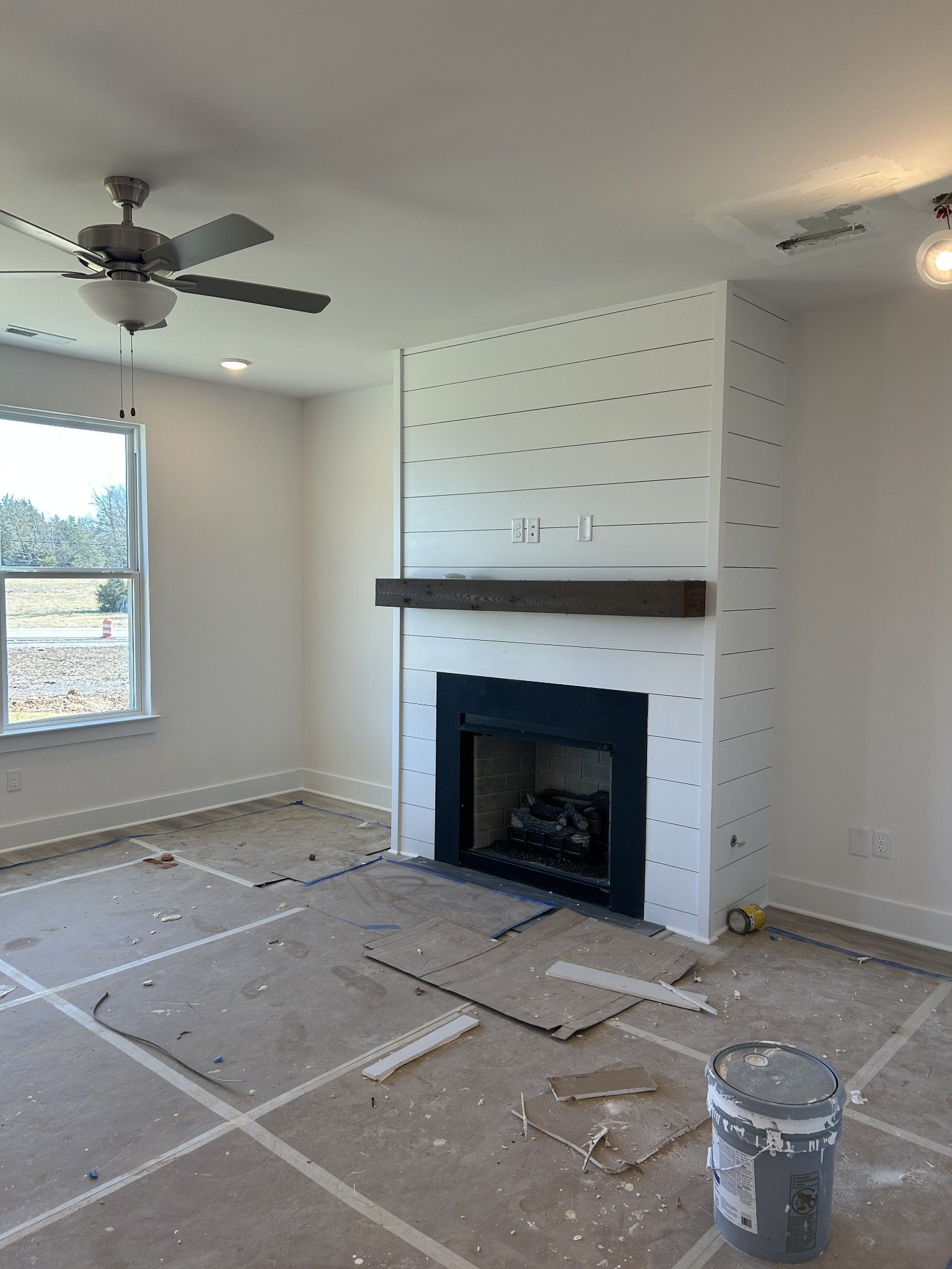 Cozy shiplap fireplace wall with black firebox, wood mantel, and ceiling fan in unfinished living room of Davidson Homes The Henry C, Mt. Juliet