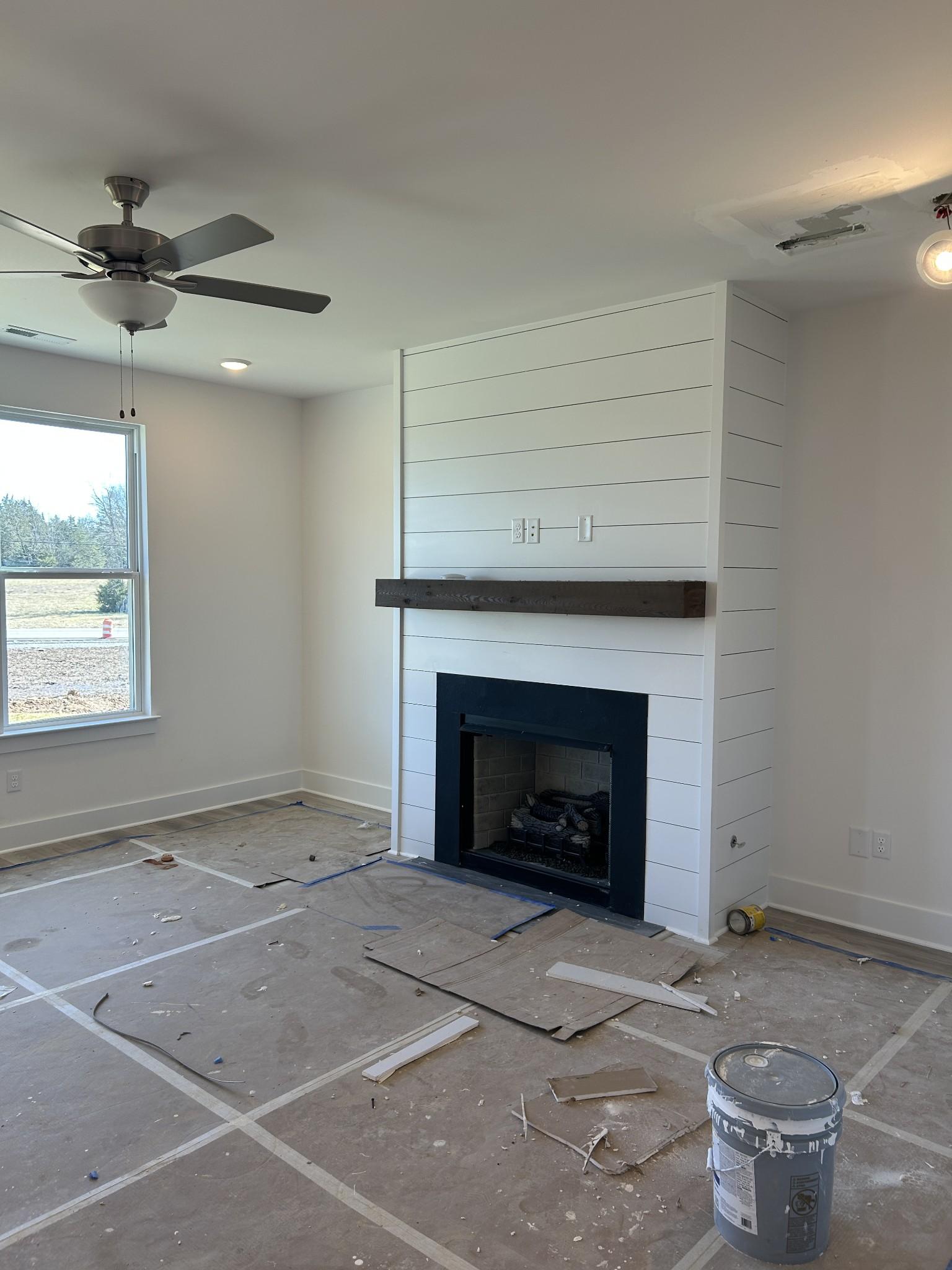 Cozy shiplap fireplace wall with black firebox, wood mantel, and ceiling fan in unfinished living room of Davidson Homes The Henry C, Mt. Juliet