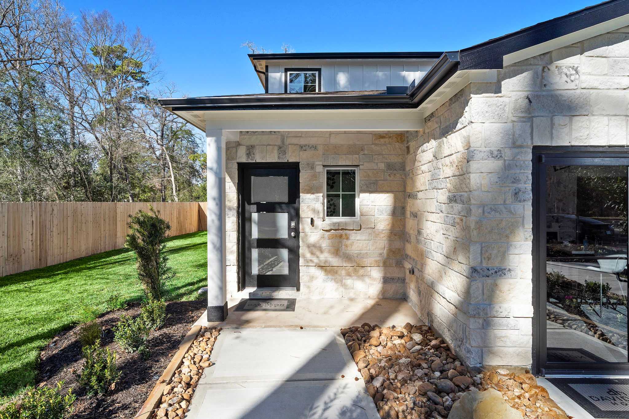 Stone facade home exterior with black door and covered porch at Lakes at Black Oak in Magnolia Texas