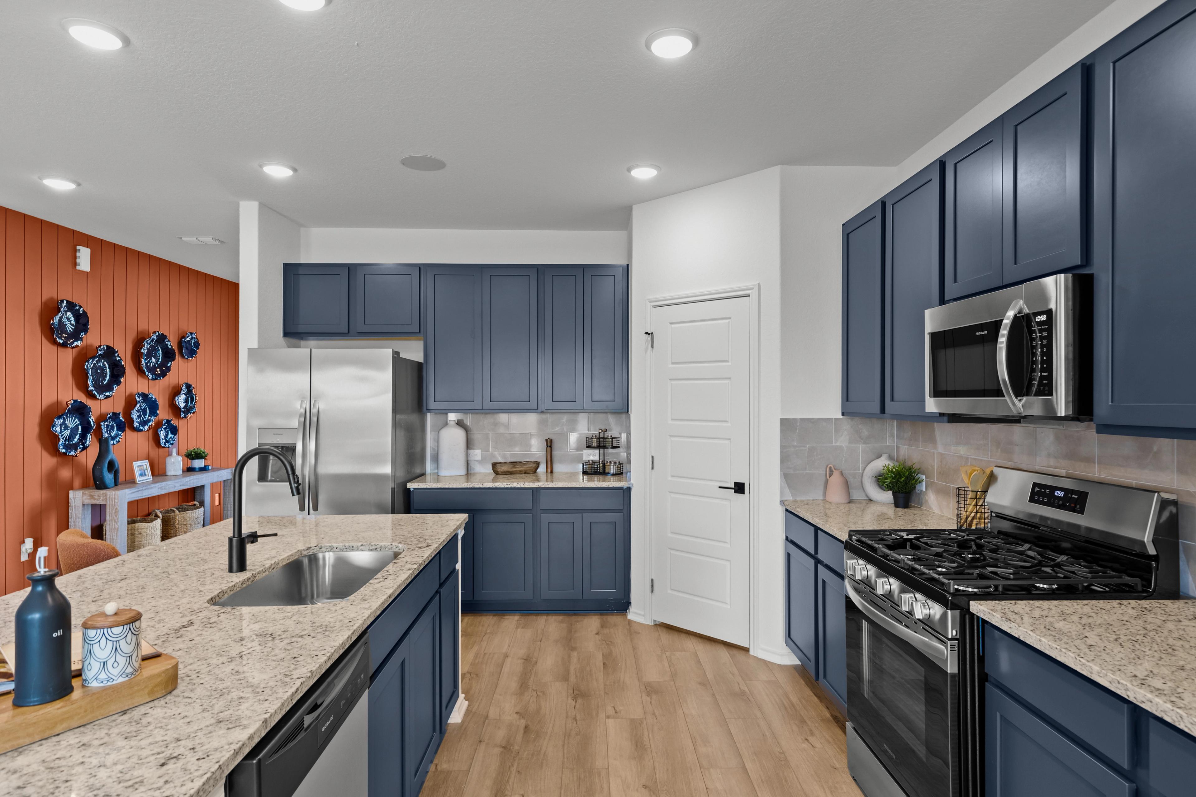 Spacious navy blue kitchen in The Douglas F with granite island, stainless steel appliances, and orange accent wall